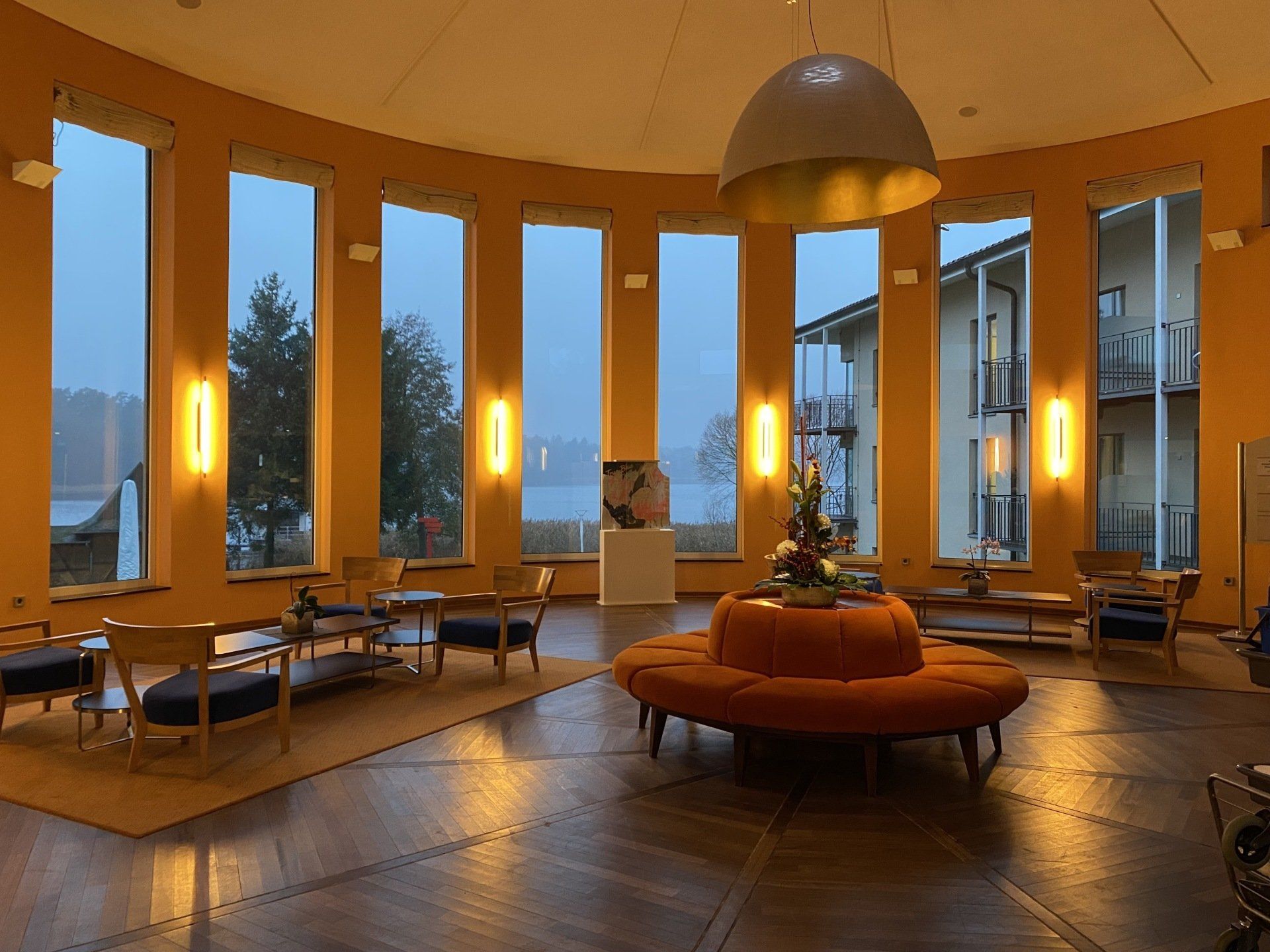 Geräumige Lobby mit geschwungenen Fenstern, Sitzgelegenheiten und einem orangefarbenen runden Sofa 