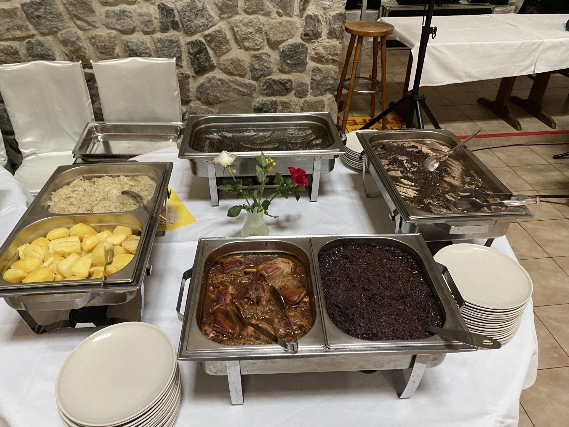 Speisebuffet mit verschiedenen Gerichten in Edelstahl-Chafing Dishes auf einer weißen Tischdecke.