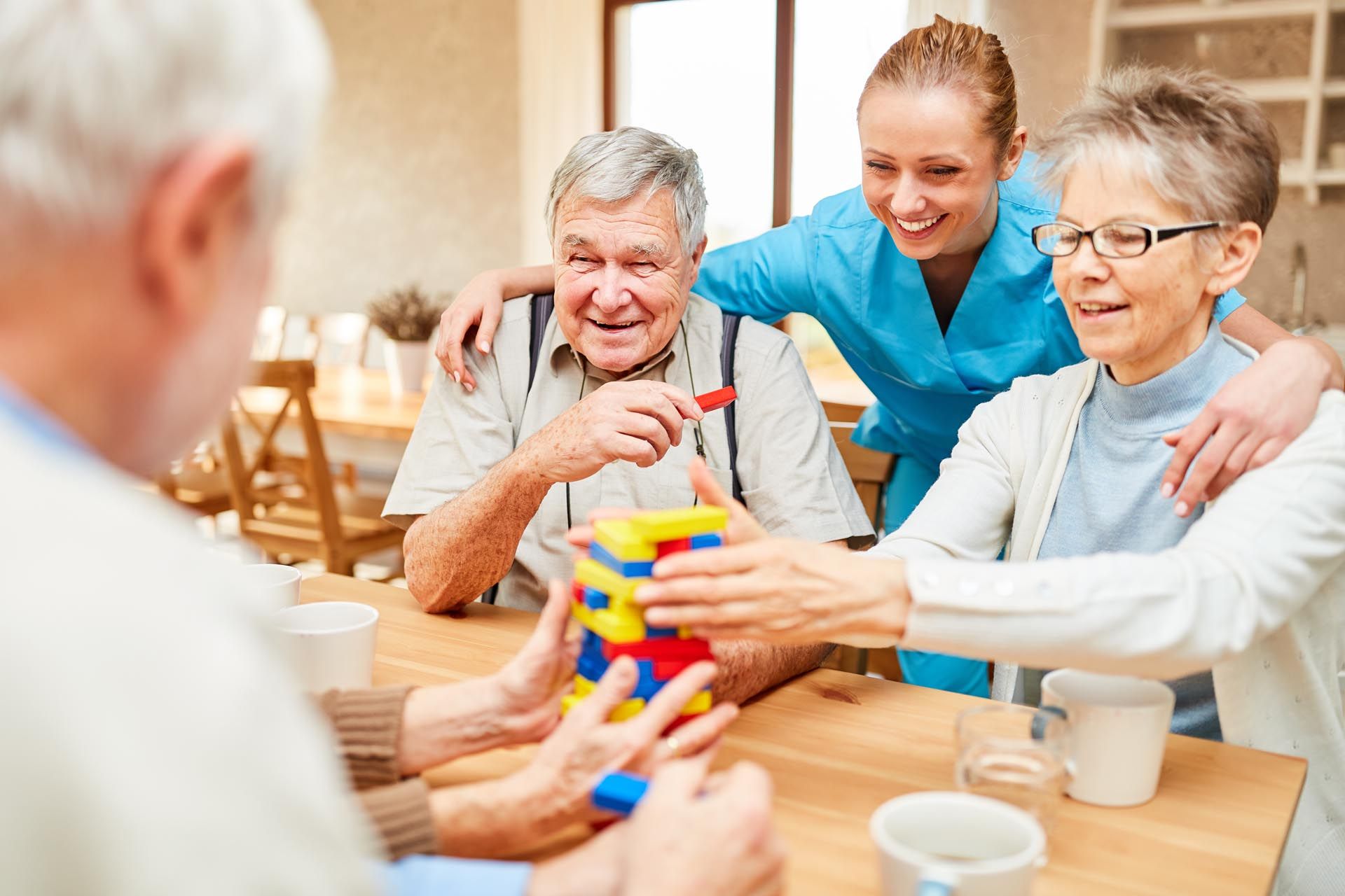 Gruppe von Menschen, die mit bunten Bauklötzen spielen, lächelnde Pflegekraft, sitzt am Tisch.