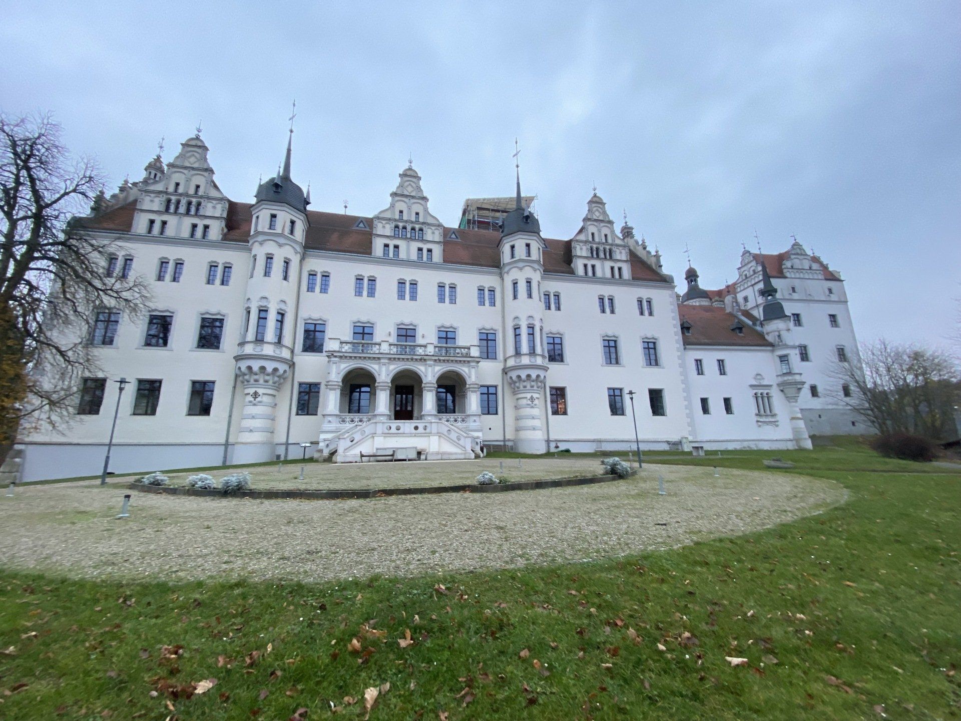Weißes Schloss mit verzierten Türmen unter einem bewölkten Himmel, von einer Rasenfläche aus gesehen.