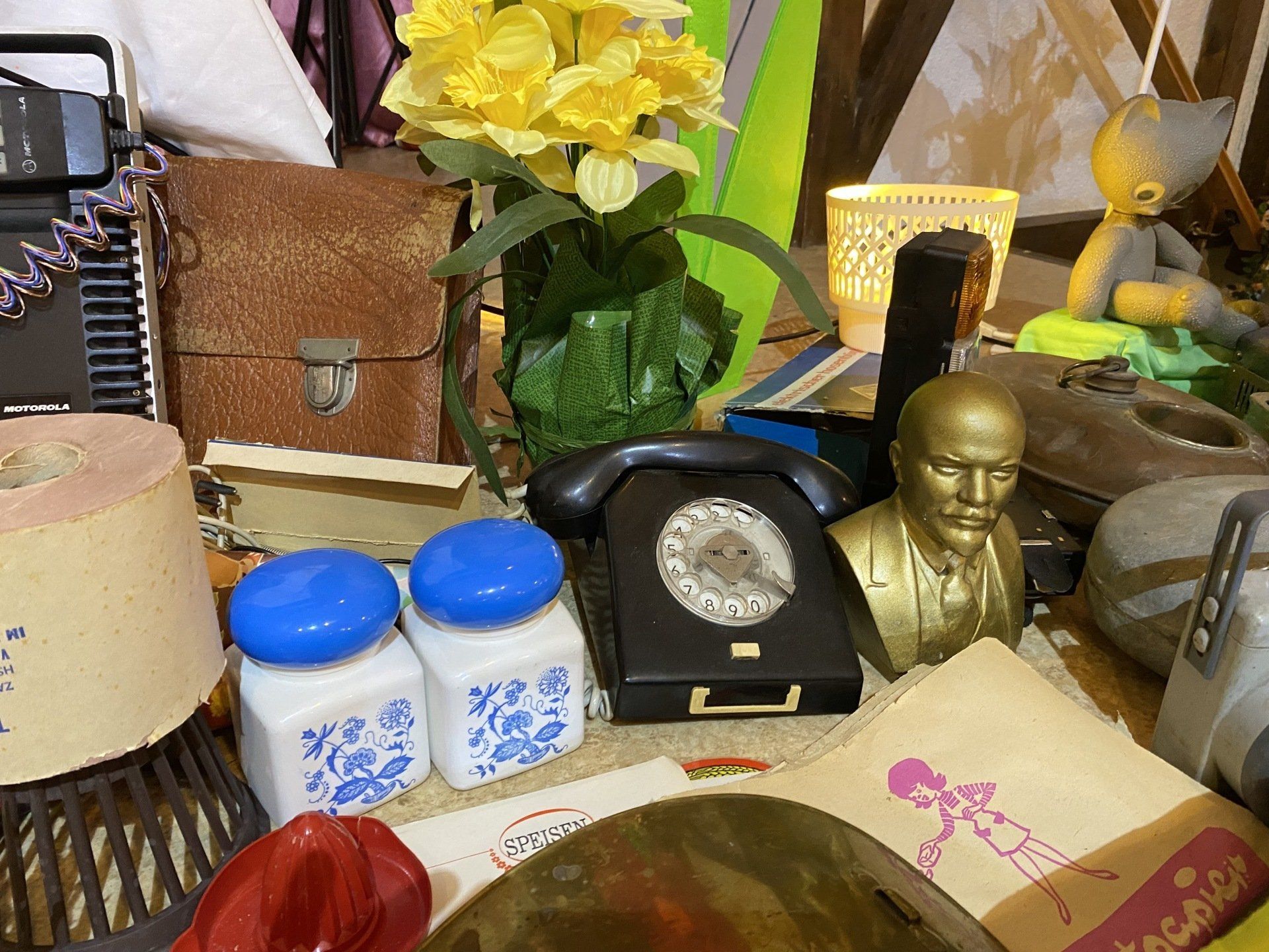 Stillleben verschiedener Objekte: ein Telefon, Blumen, eine Büste und andere Gegenstände.