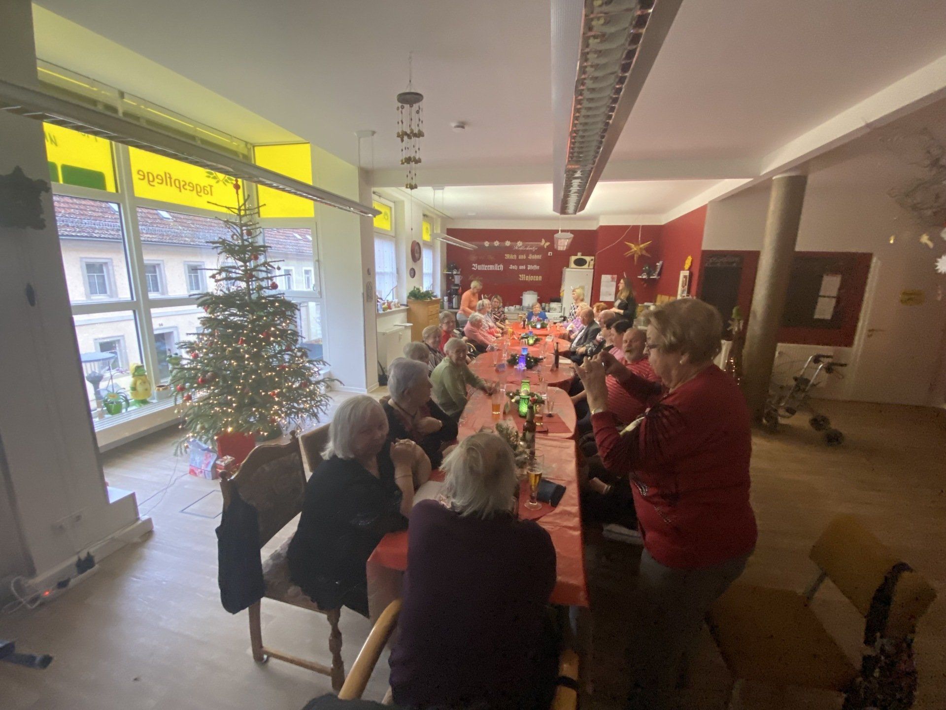 Menschen sitzen an einem langen Tisch und feiern, in der Nähe steht ein Weihnachtsbaum.