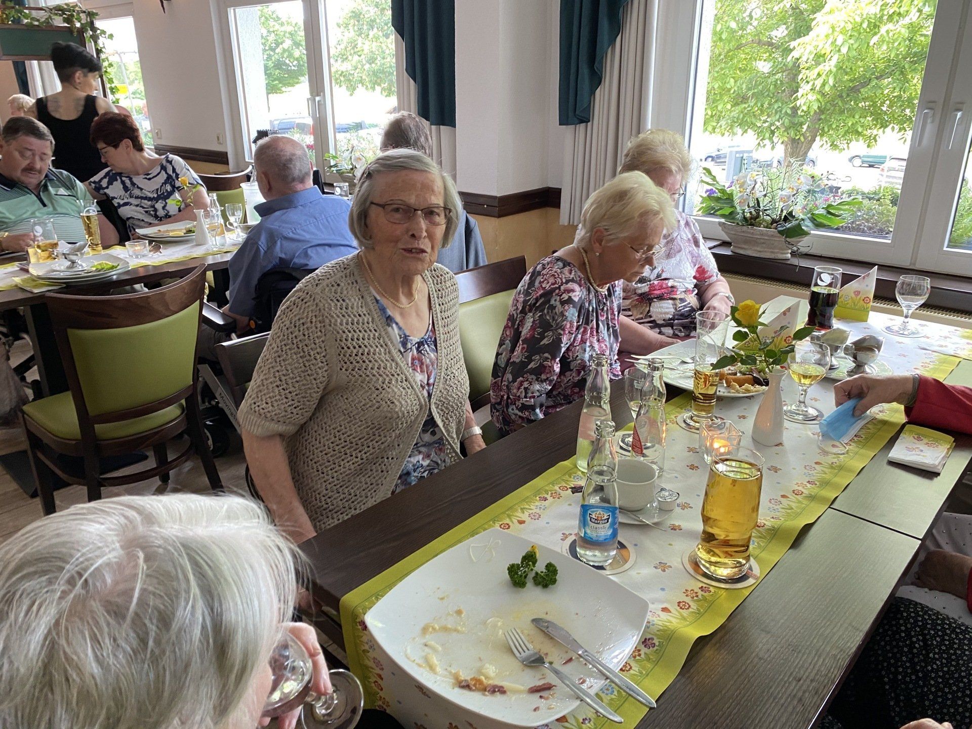 Menschen sitzen an Tischen in einem Restaurant; einige schauen in die Kamera.