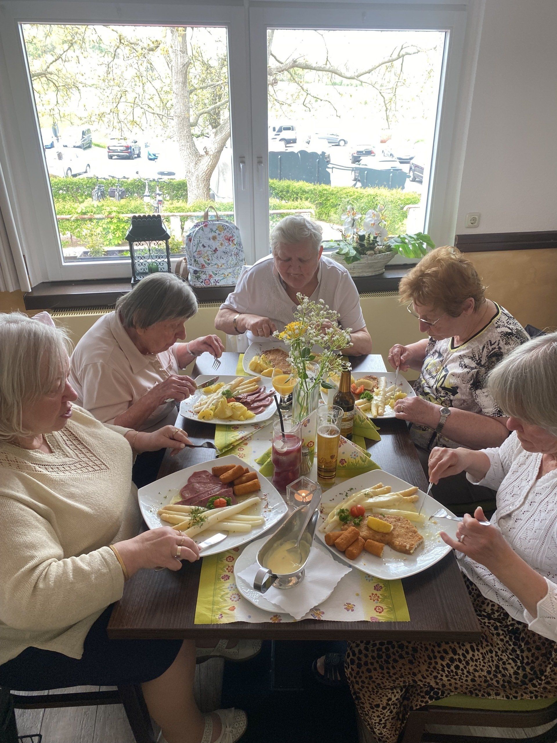 Fünf Frauen sitzen an einem Tisch und essen in einem gut beleuchteten Raum, möglicherweise einem Restaurant.