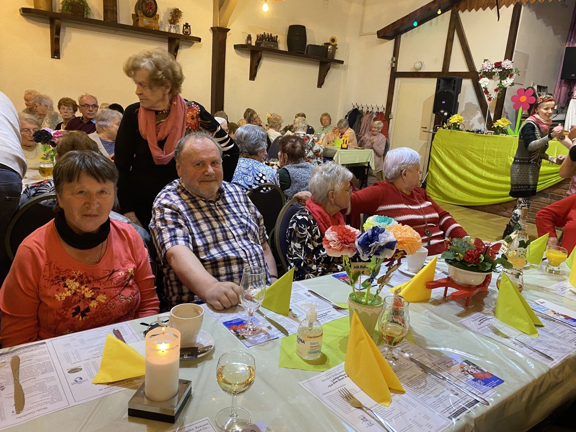 Menschen sitzen an einem festlich gedeckten Tisch, eine Kerze und Gläser sind zu sehen.
