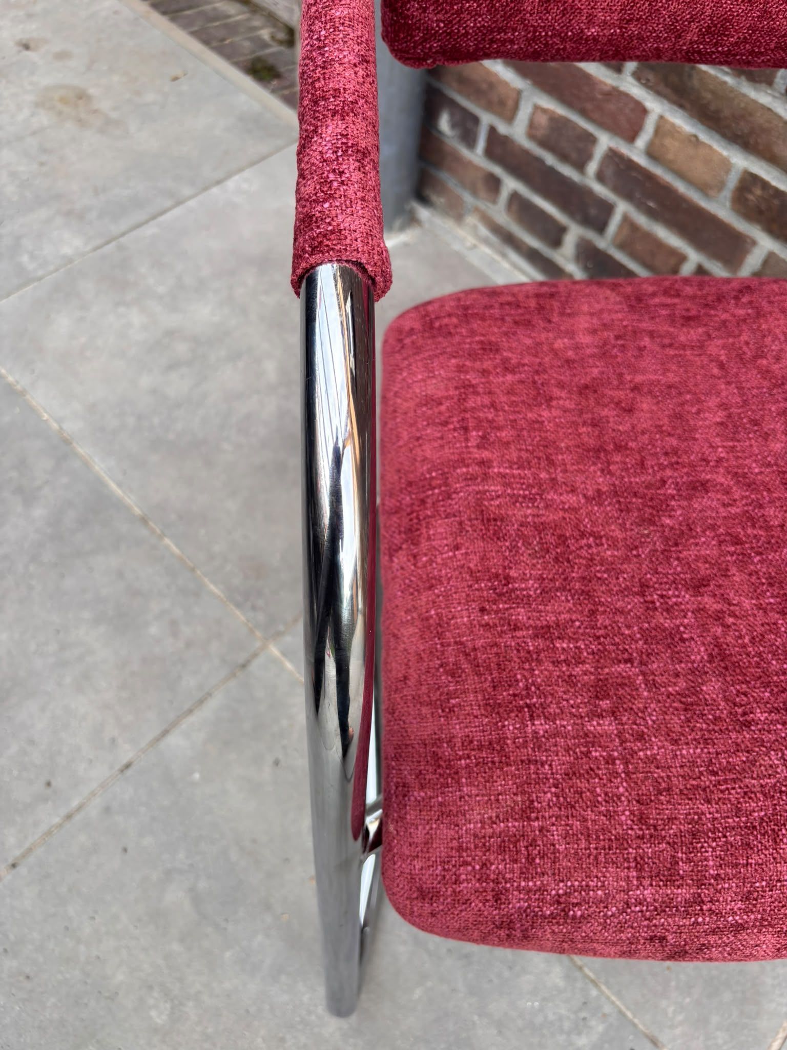 Rode gestoffeerde stoel met een verchroomd buisframe en armleuningen op een witte achtergrond
