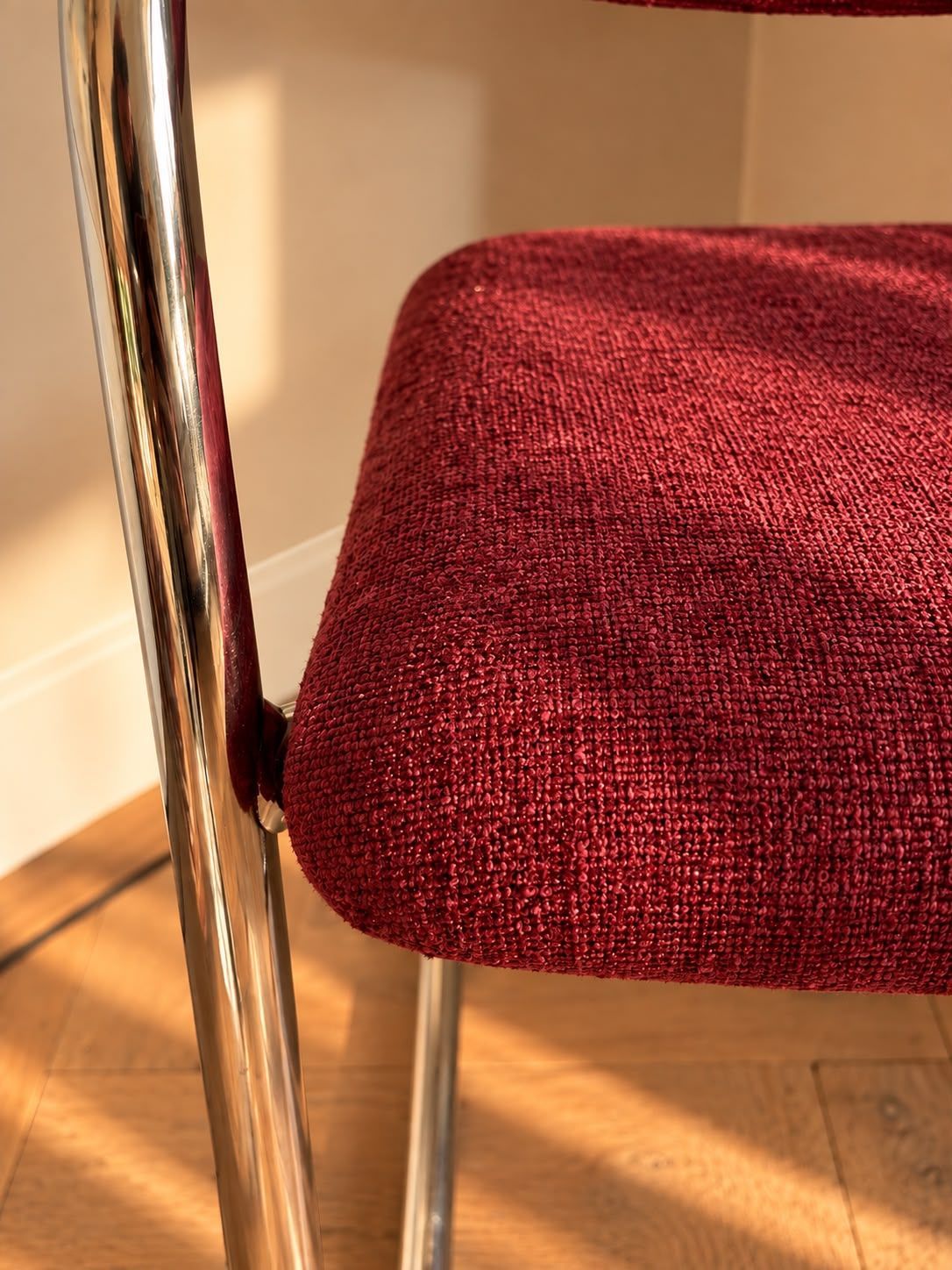 Bordeauxrode fauteuil met bekleding, een chromen frame, in een hoek naast gordijnen en wanddecoratie