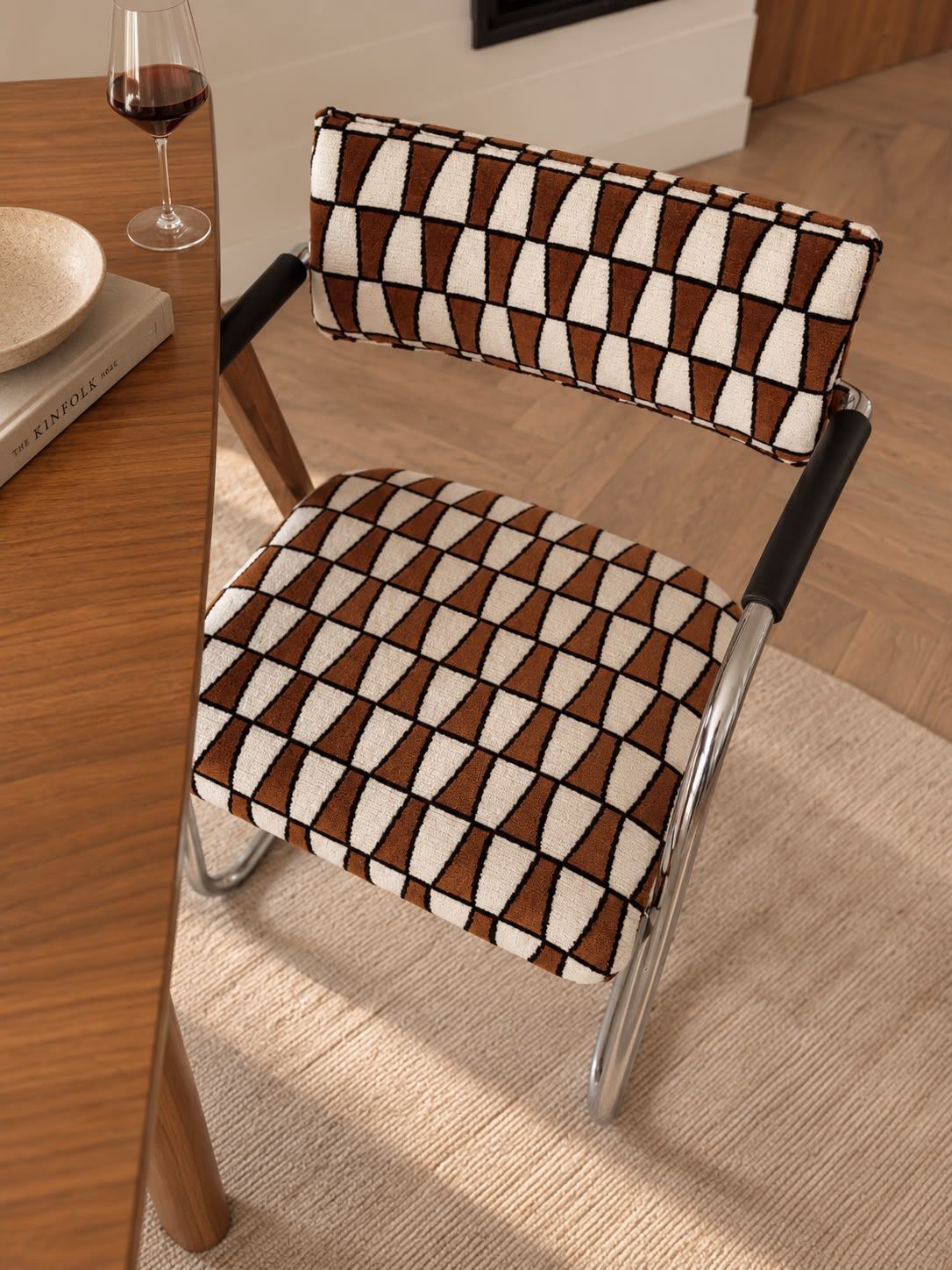 Moderne stoel bij een houten tafel in een zonnige, minimalistische eetkamer, met een wijnglas en een vaas op tafel