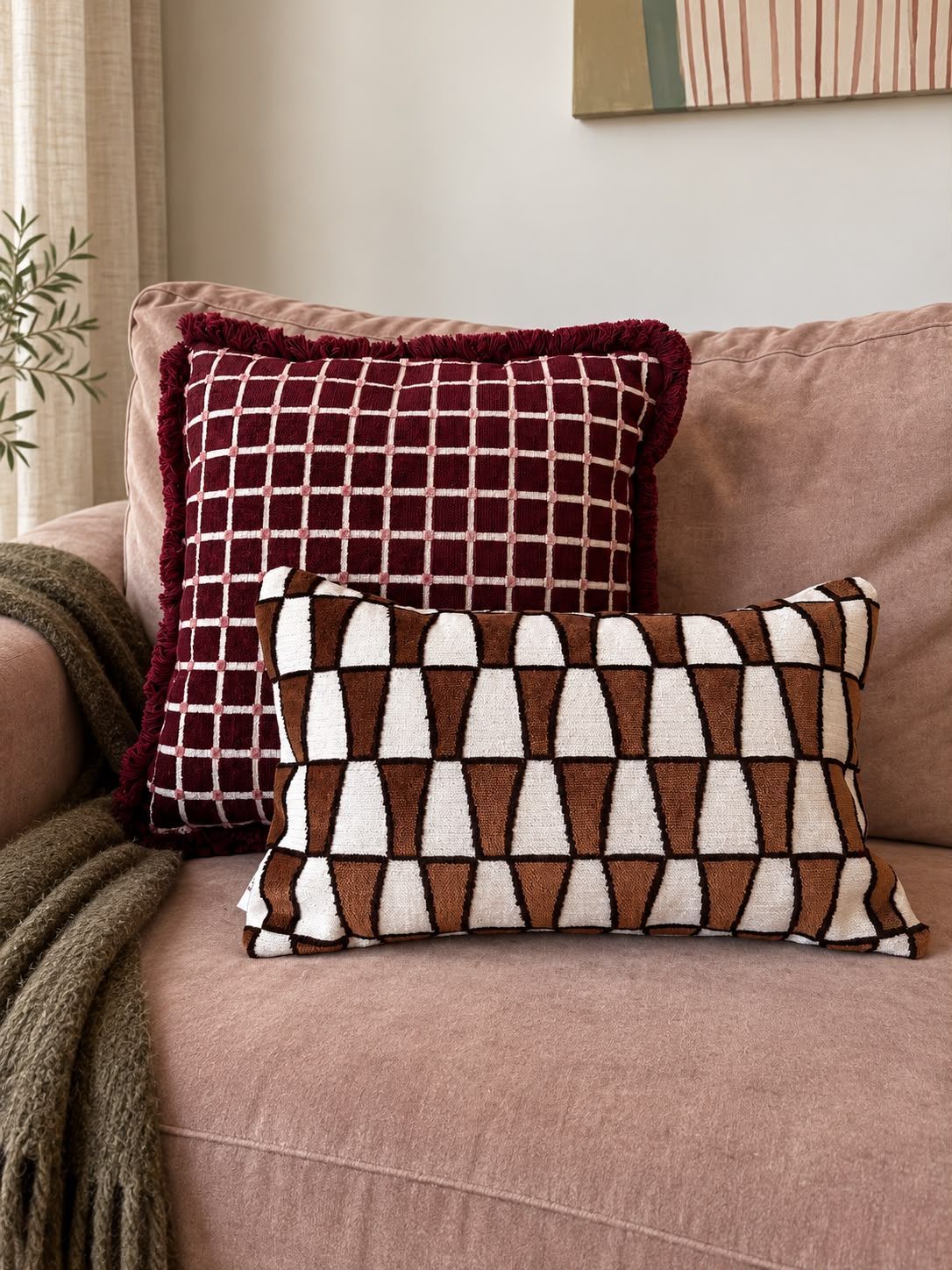 Roze bank met een bruin-wit geometrisch sierkussen en een gedrapeerde deken in een knusse woonkamer