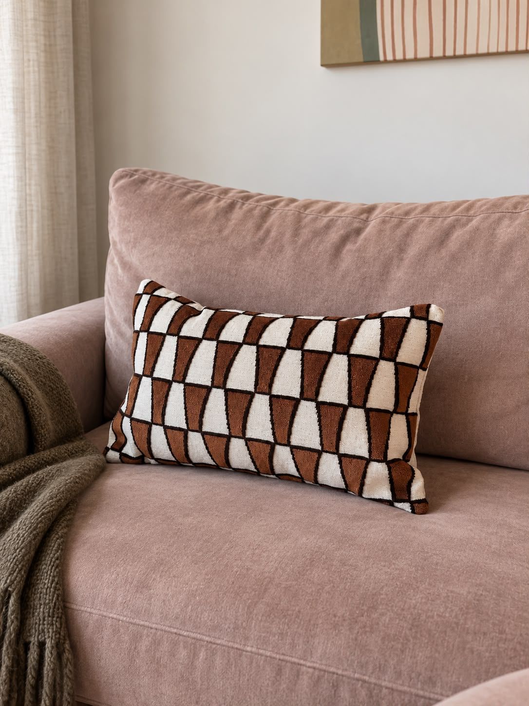 Roze bank met een bruin-wit geometrisch sierkussen en een gedrapeerde deken in een knusse woonkamer