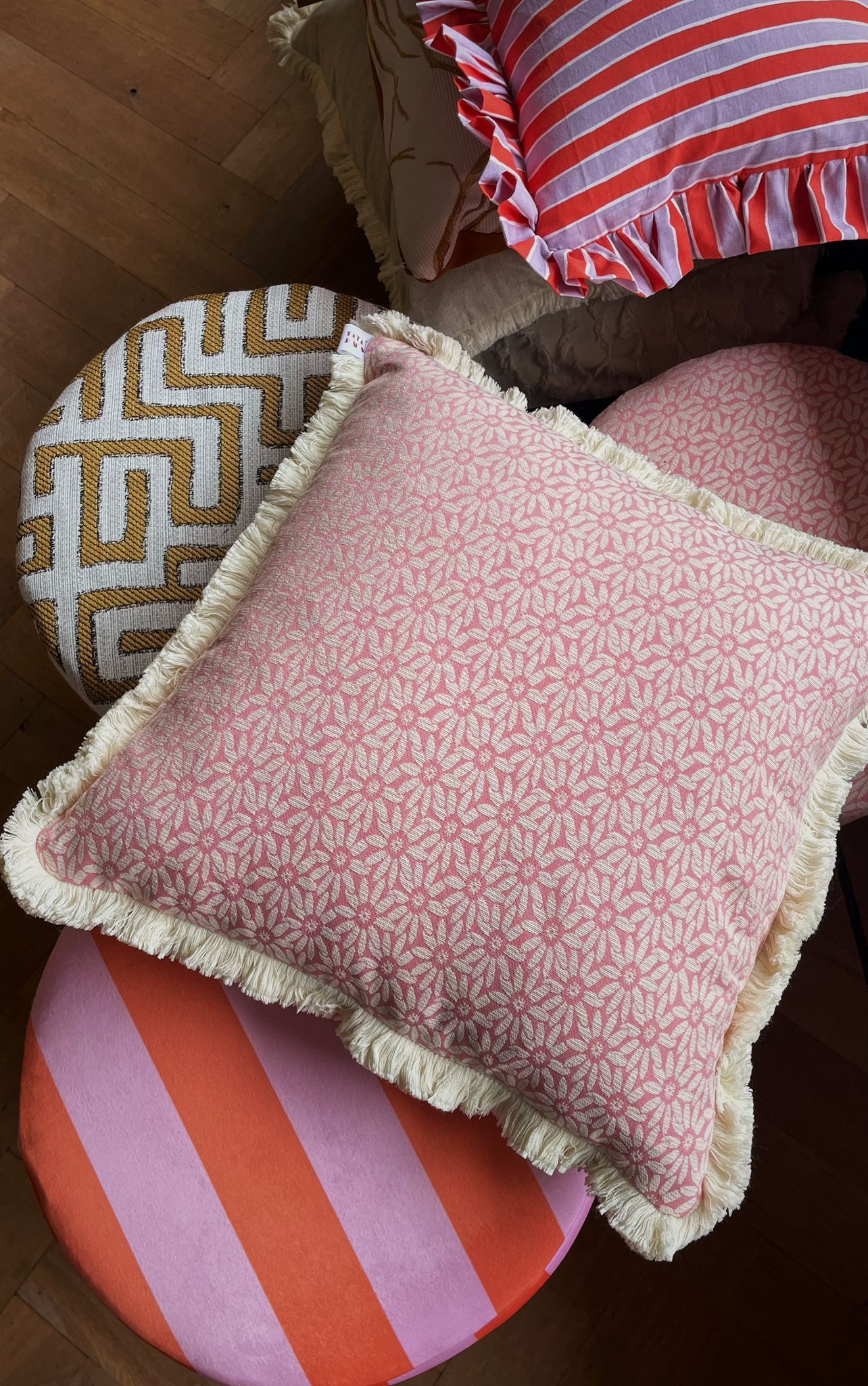 Roze vierkant sierkussen met patroon en een beige rand op een witte achtergrond.