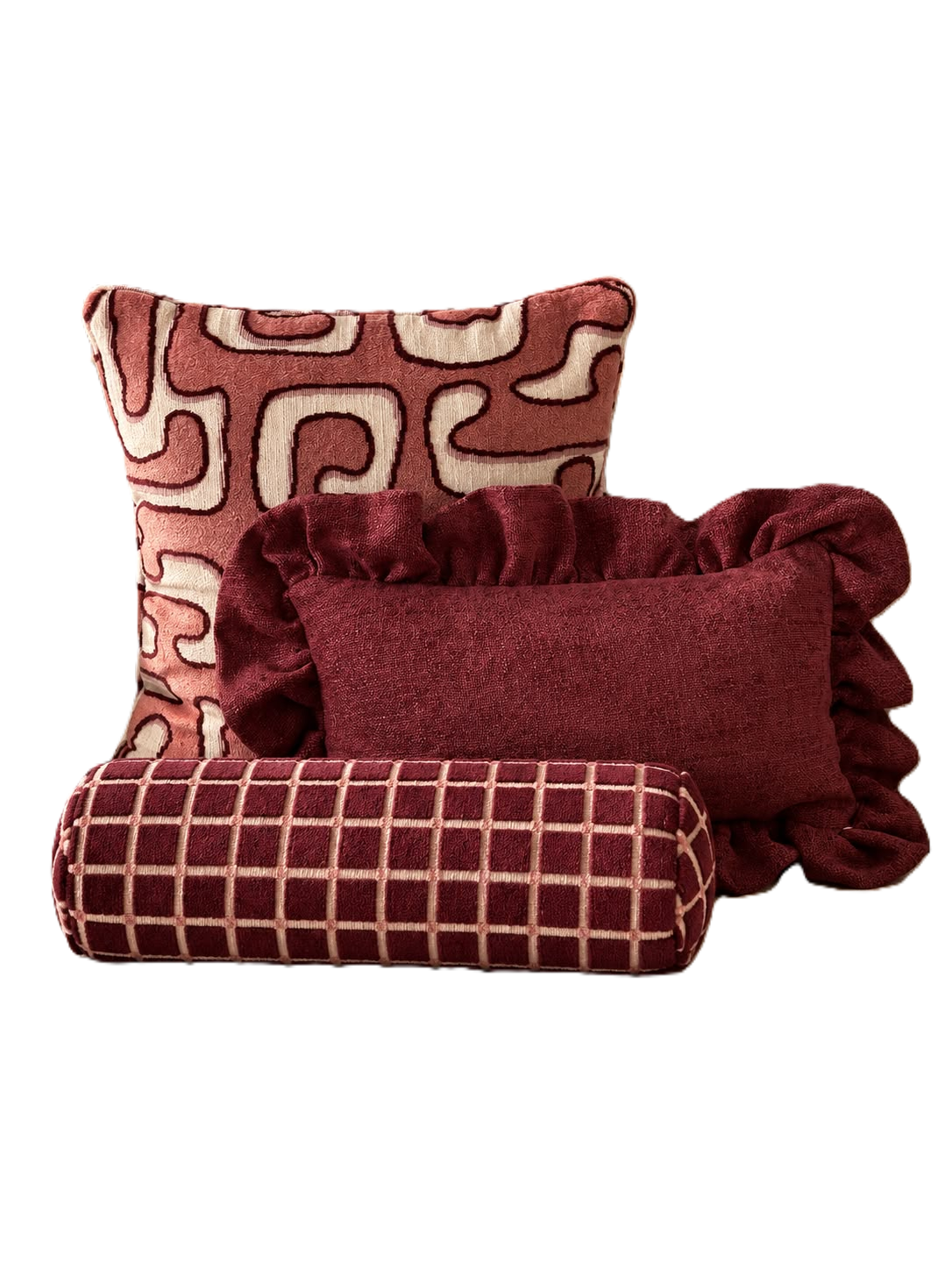 Drie sierkussens met geometrische patronen in bordeauxrood, crème en rood.