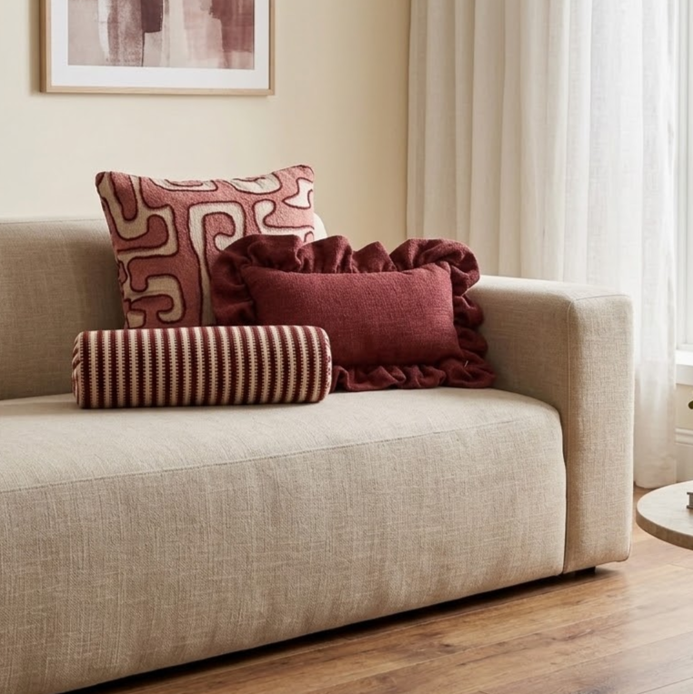 Drie decoratieve sierkussens in rood en crème met verschillende patronen, opgestapeld