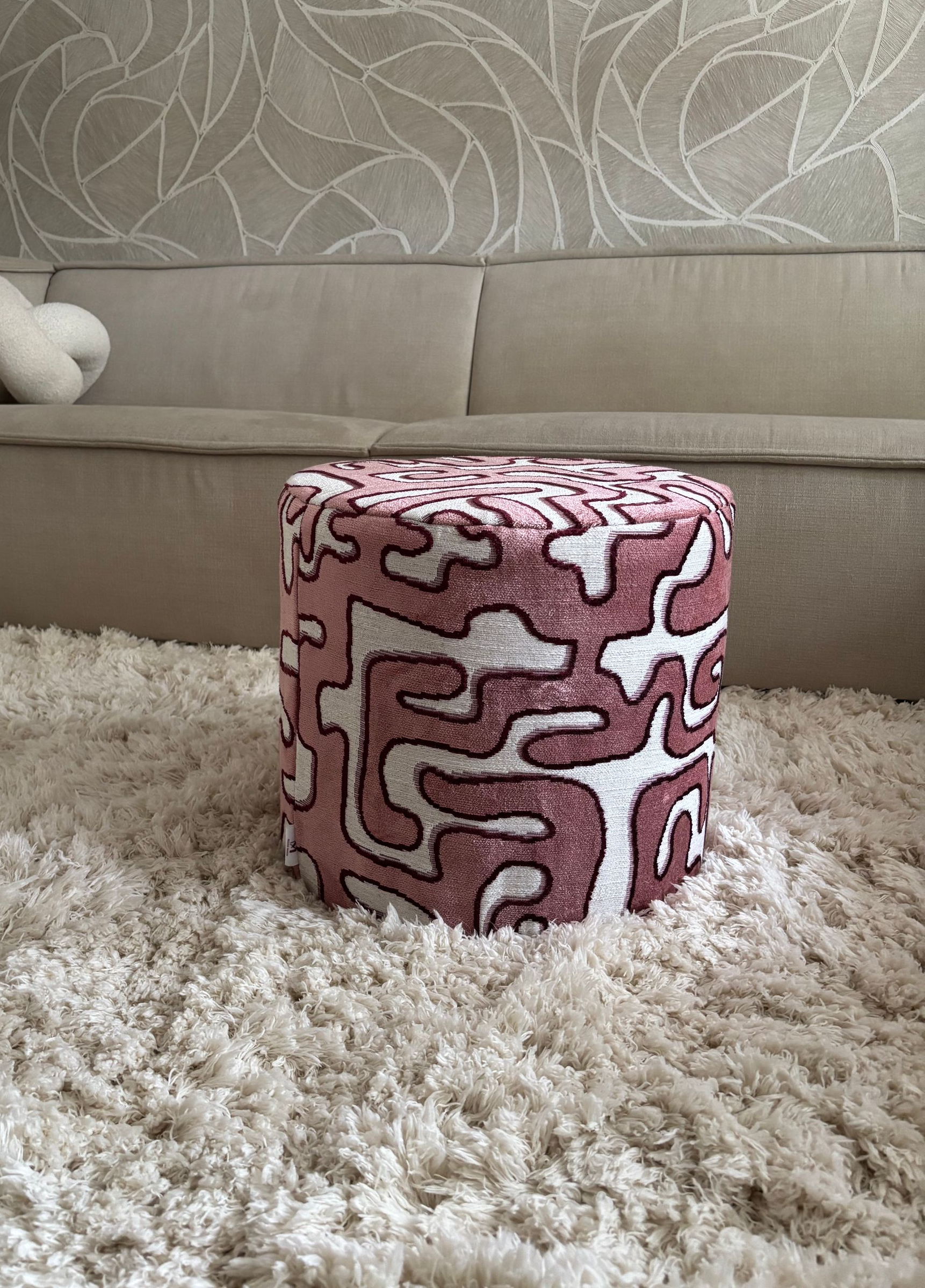 Roze poef met patroon op een zacht wit vloerkleed voor een beige bank.