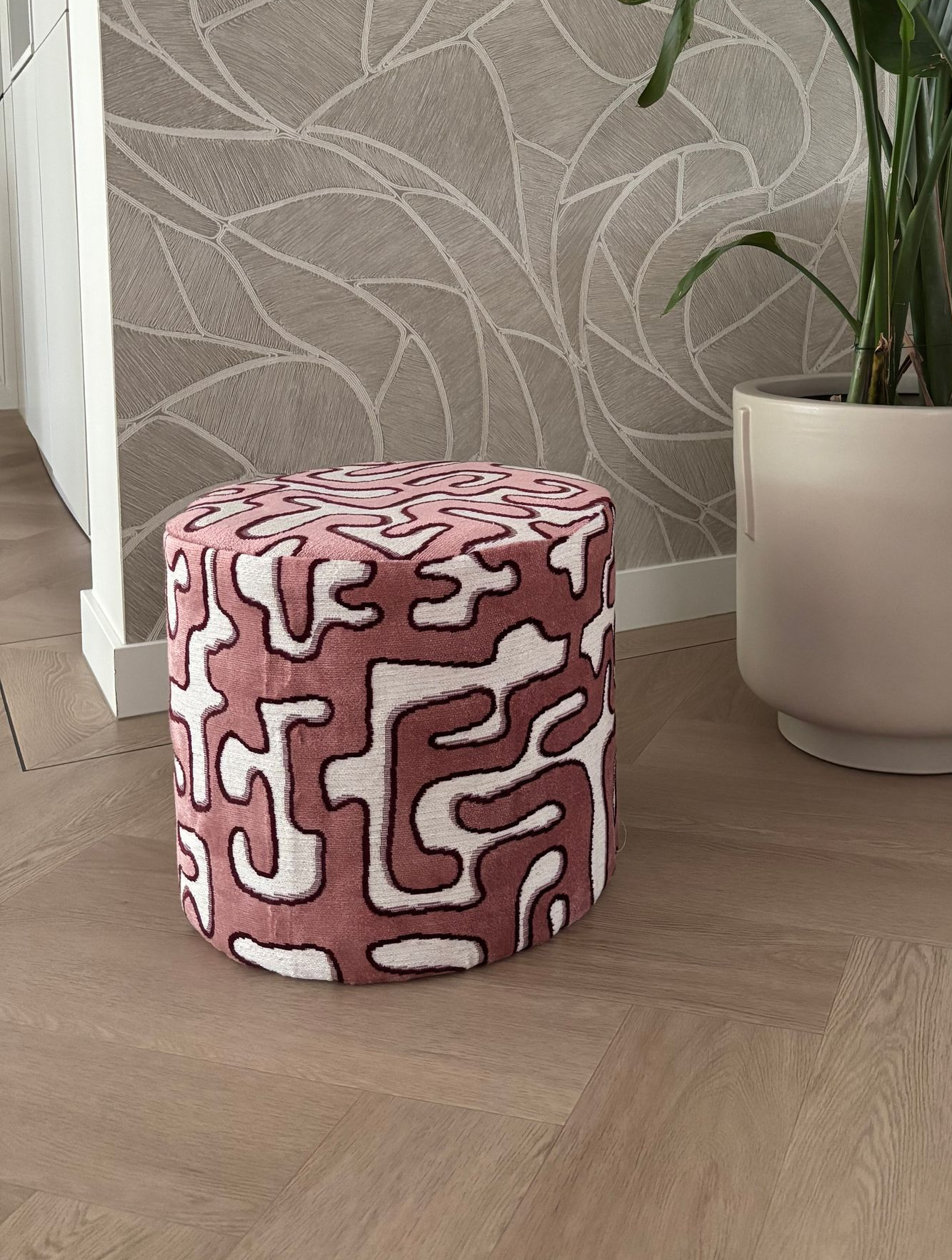 Roze poef met patroon op een zacht wit vloerkleed voor een beige bank.