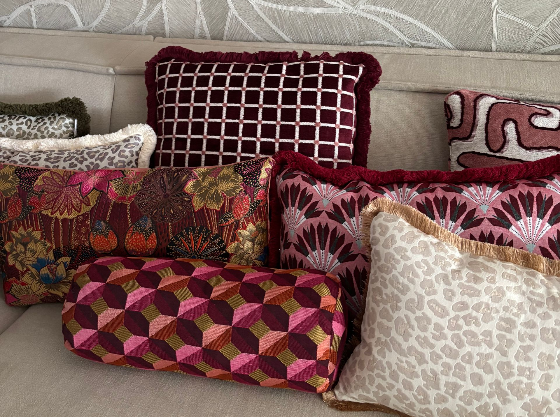 Decoratieve kussens met rode, roze en beige patronen liggen op een bank.