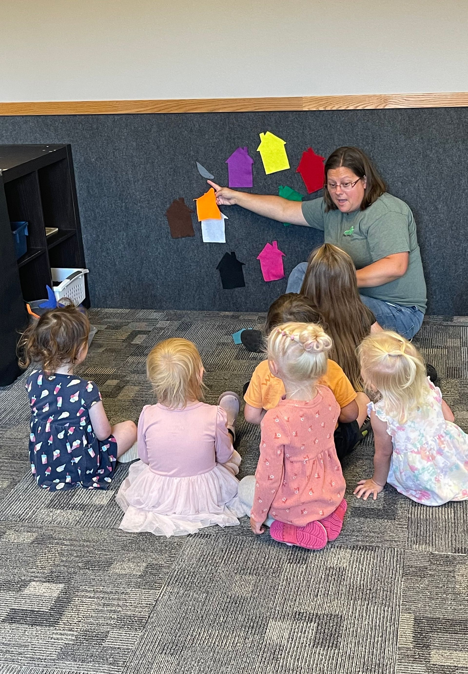 A woman is sitting on the floor talking to a group of children.