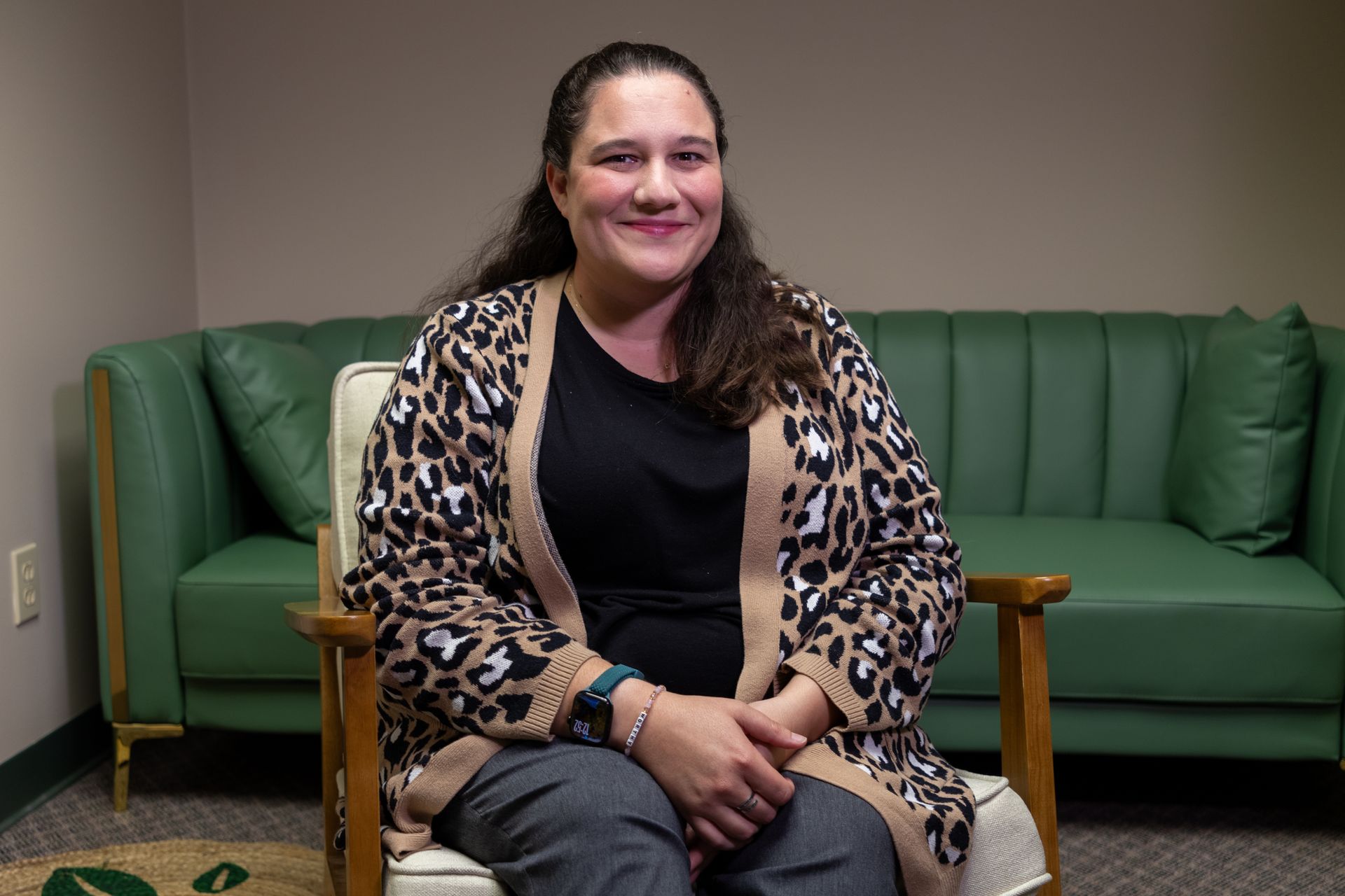 Image of clinician Meaghan Viggiani smiling warming in a well lit office environment sitting in a white chair with a green couch behind her.