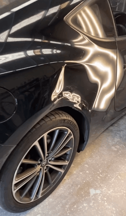 A black car with a damaged fender is parked in a garage.