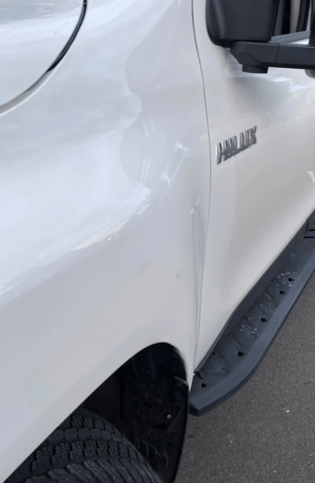 A white hilux truck is parked on the side of the road getting dent repairs.
