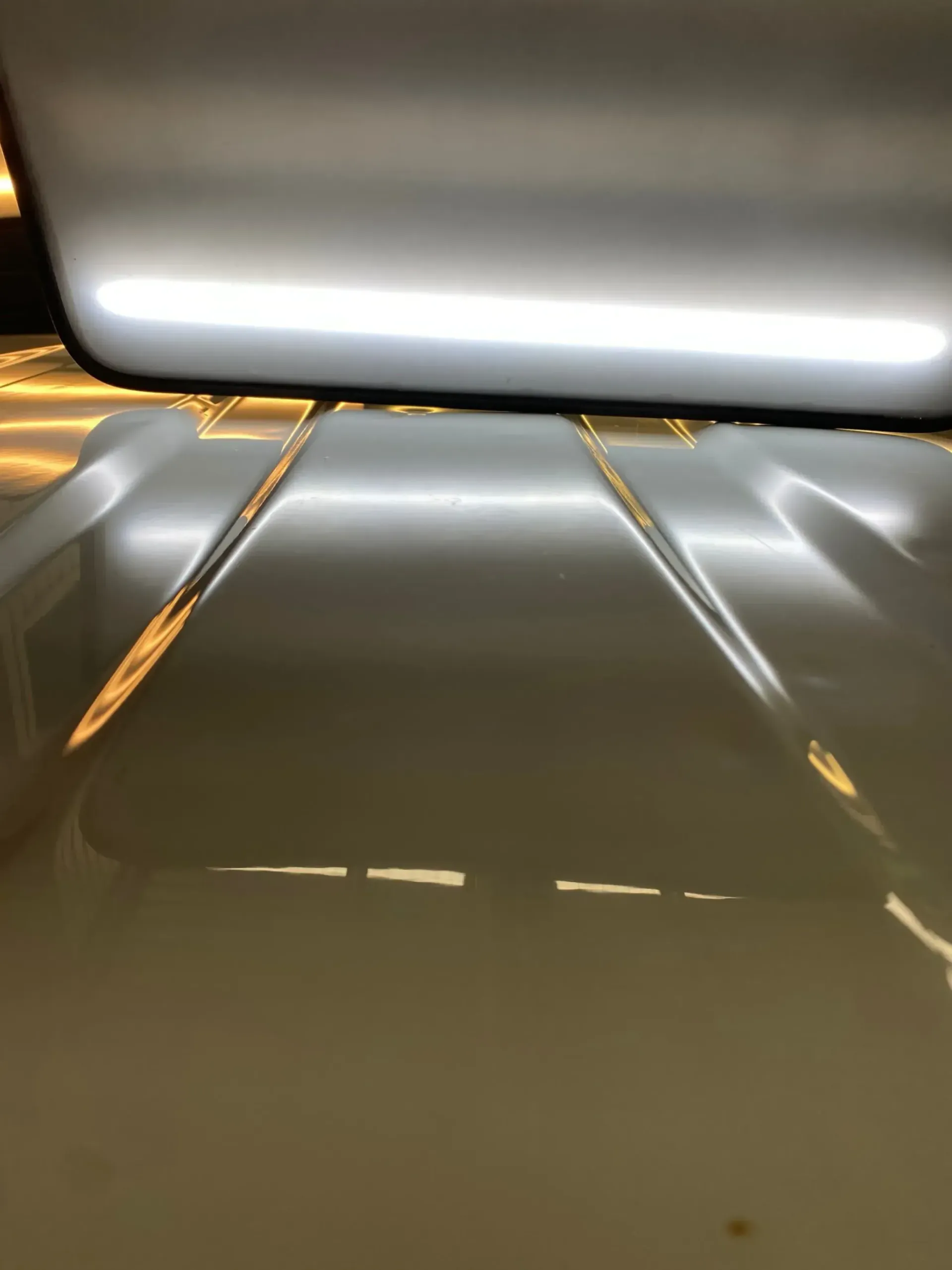 A close up of a white car hood with a light shining on it, with dents removed.