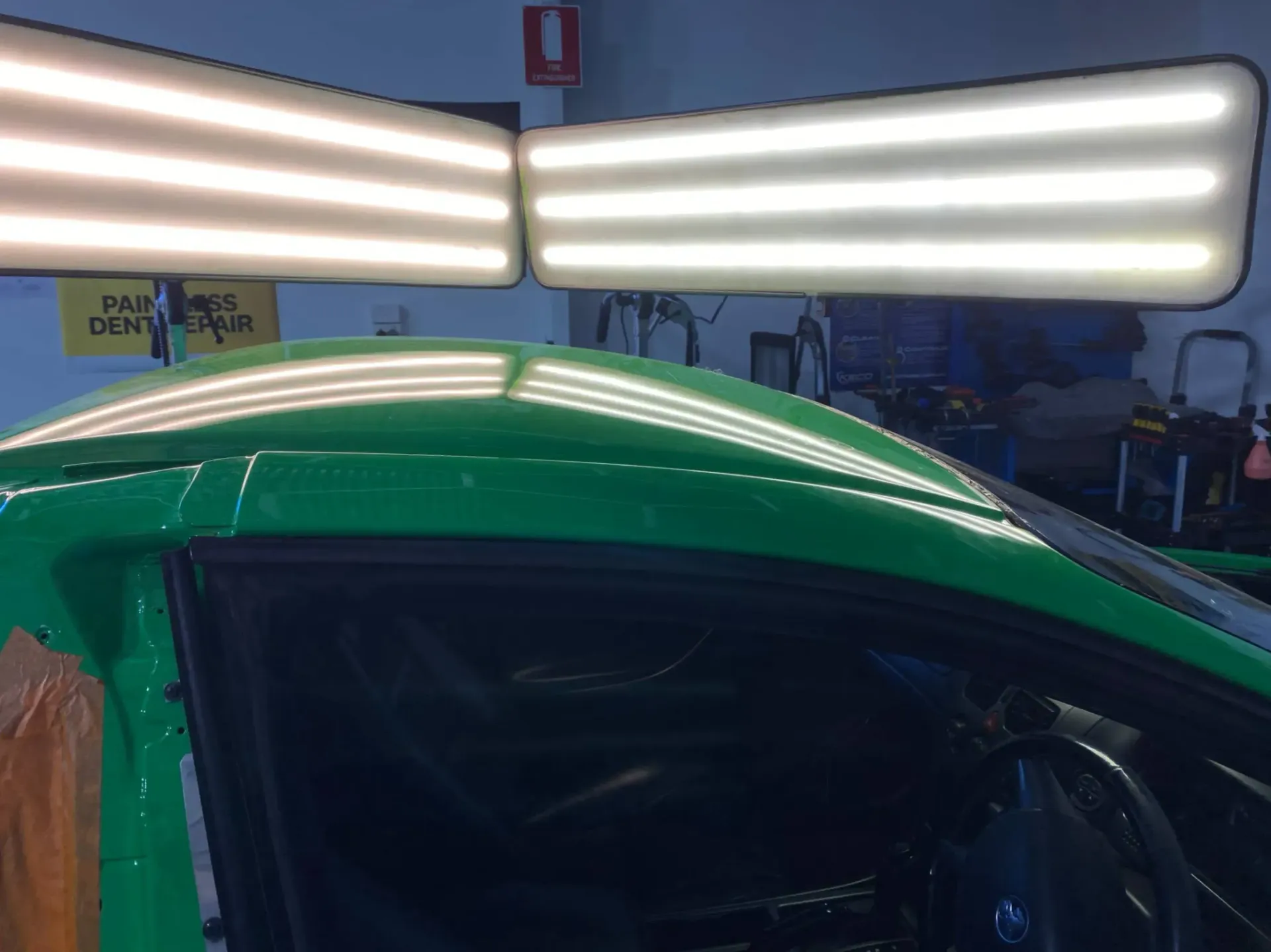 A green car is sitting in a garage with a lot of lights on it after dents removed.