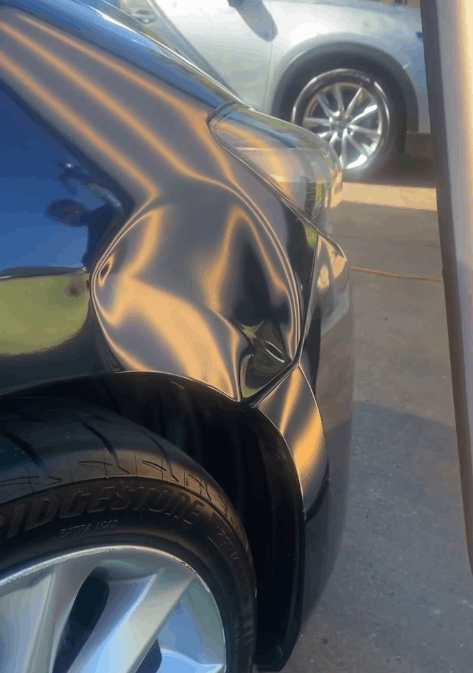 A car with a damaged fender is parked in a parking lot