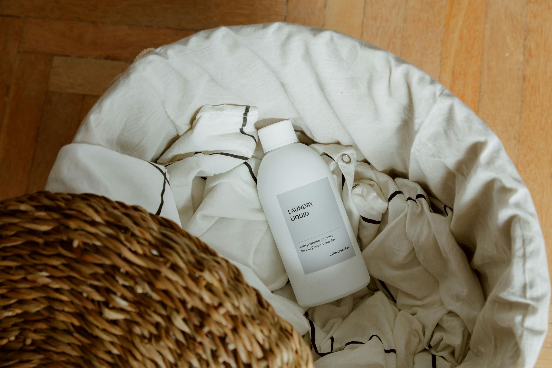 White bottle lying in a fabric basket on a wooden floor, with woven wicker visible at left