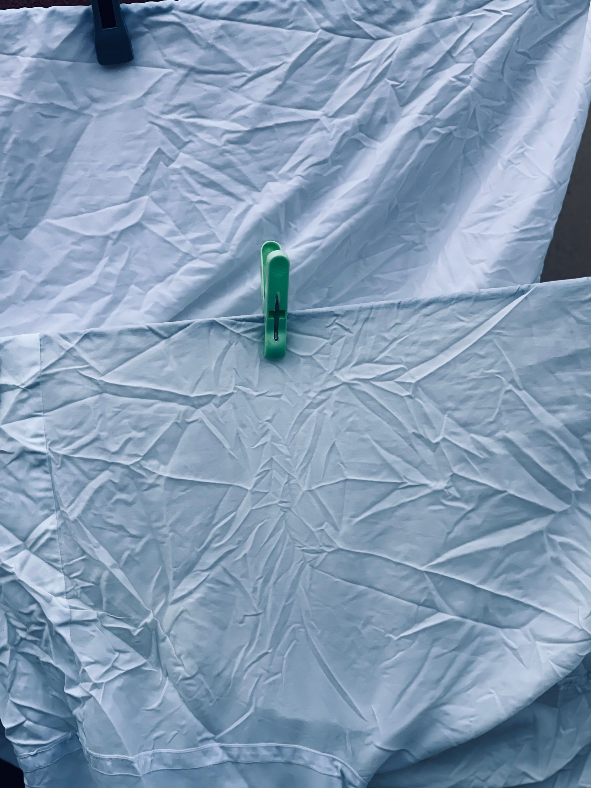 Green clothespin clipped to wrinkled gray fabric on a clothesline