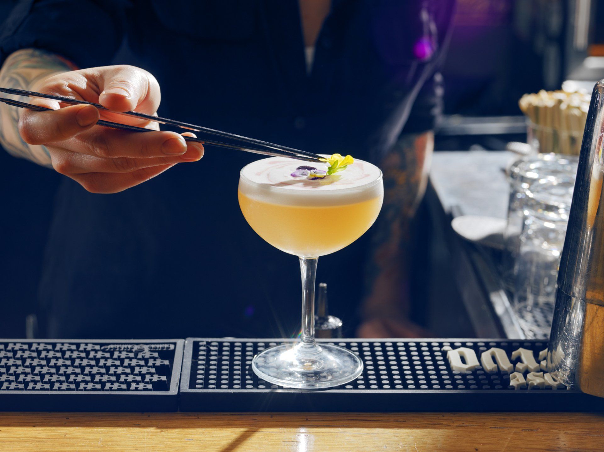 Hand stirring a pale yellow cocktail in a martini glass on a bar counter