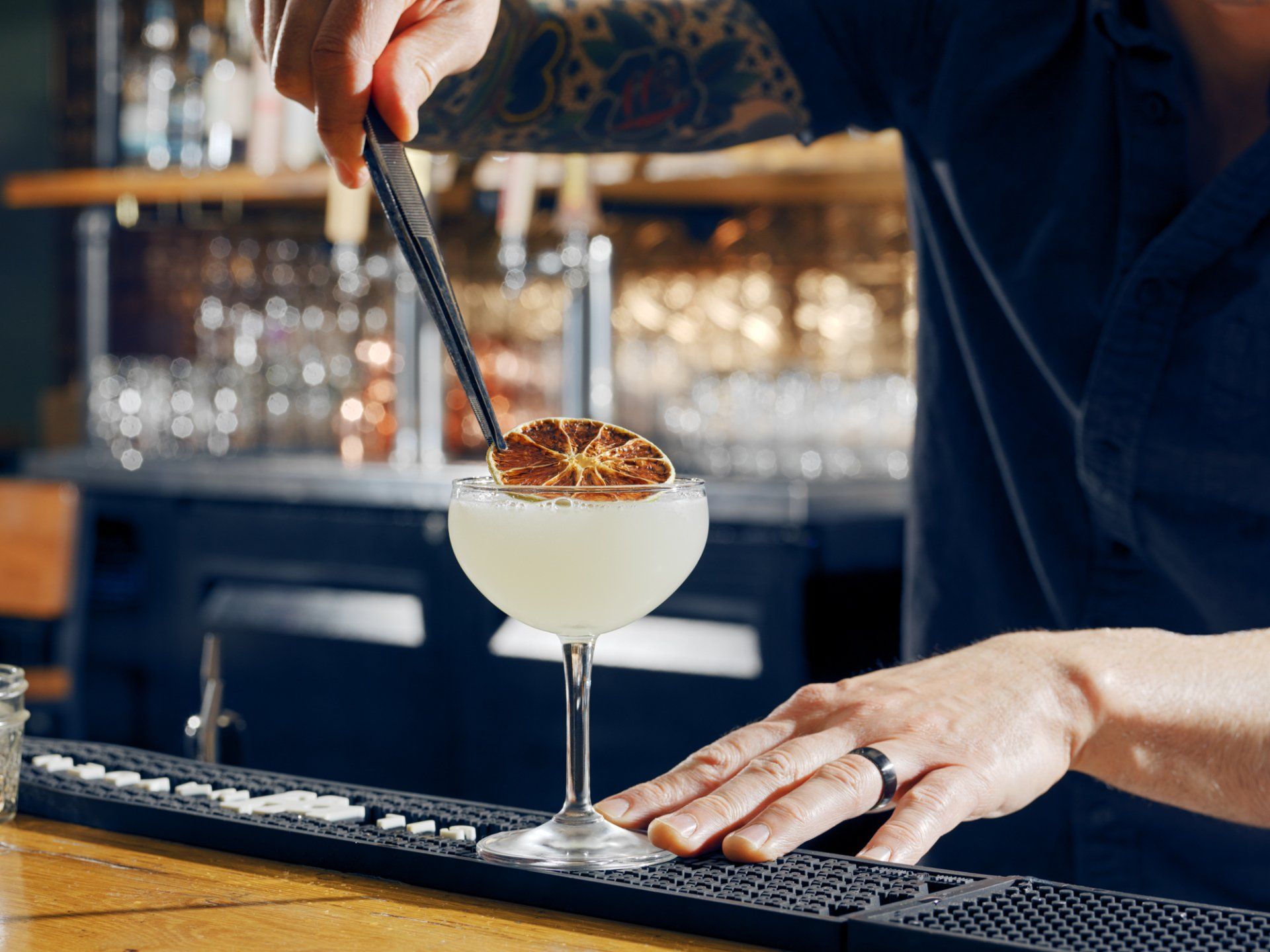 Bartender garnishing a cocktail in a coupe glass behind a bar.