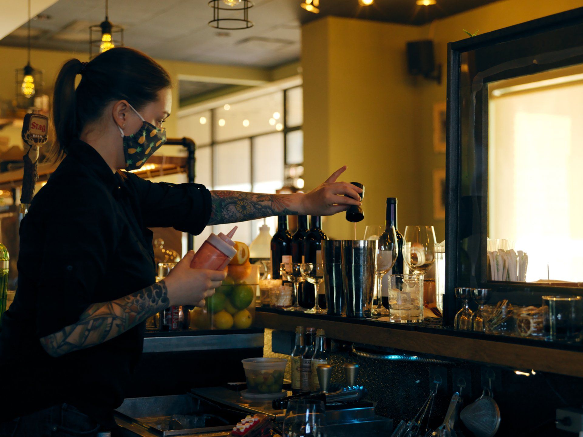 Bartender preparing drinks behind a bar, reaching for bottles in a warmly lit lounge.