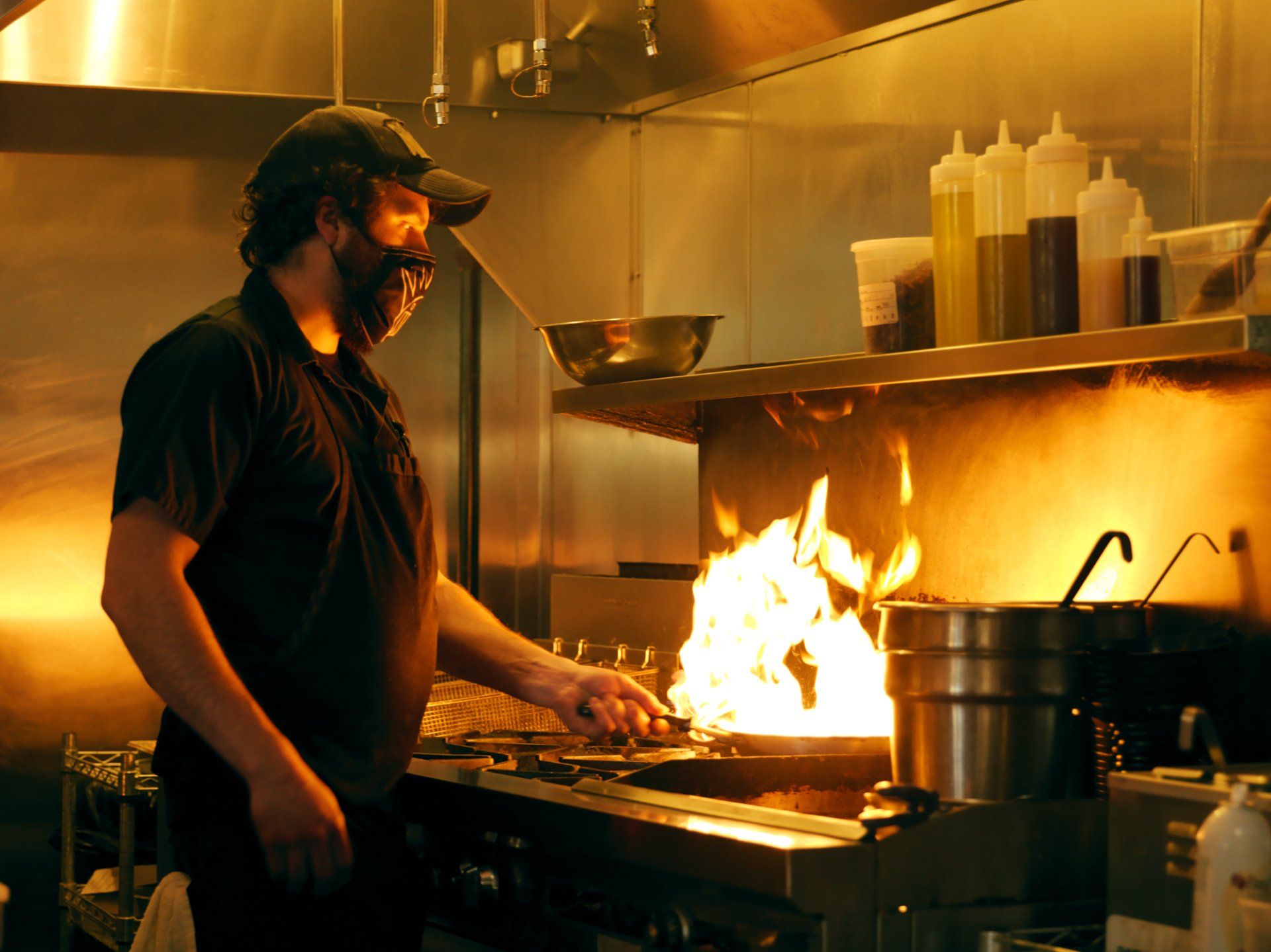 Chef cooking at a flaming stovetop in a warm-lit commercial kitchen