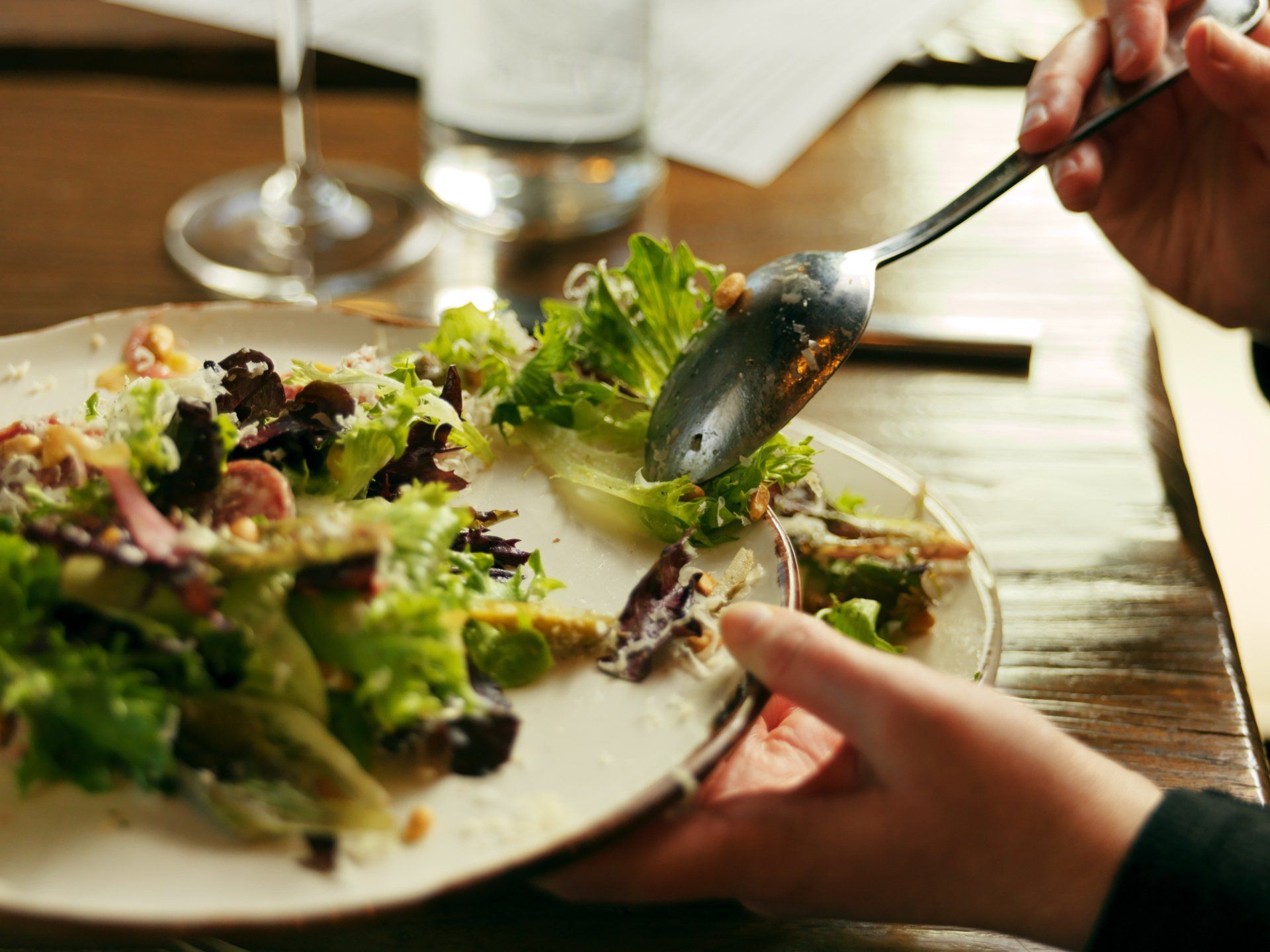Hands serving a salad on a plate at a restaurant table