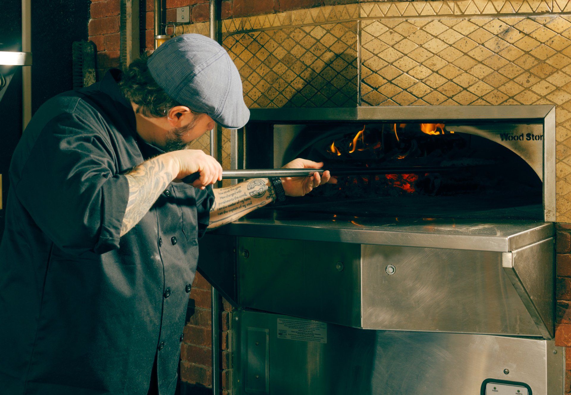 Person placing a pizza into a wood-fired oven with a peel in a restaurant kitchen