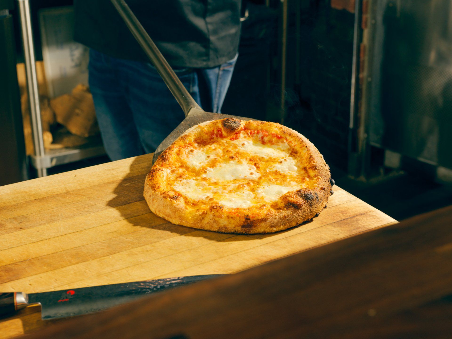 A freshly baked pizza on a wooden peel in a kitchen oven area