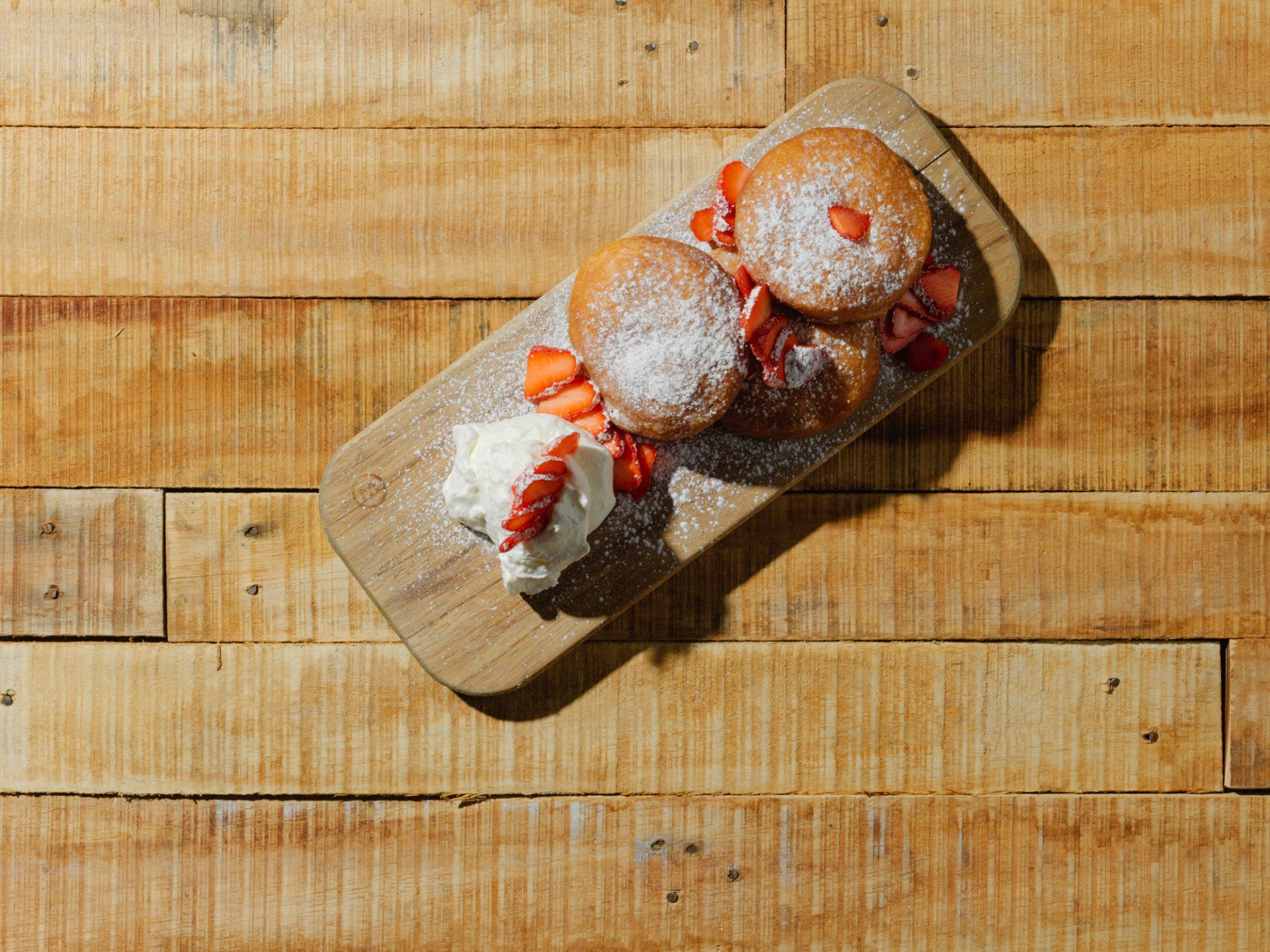 Donuts and strawberry-topped pastries on a wooden board over a rustic wood table.