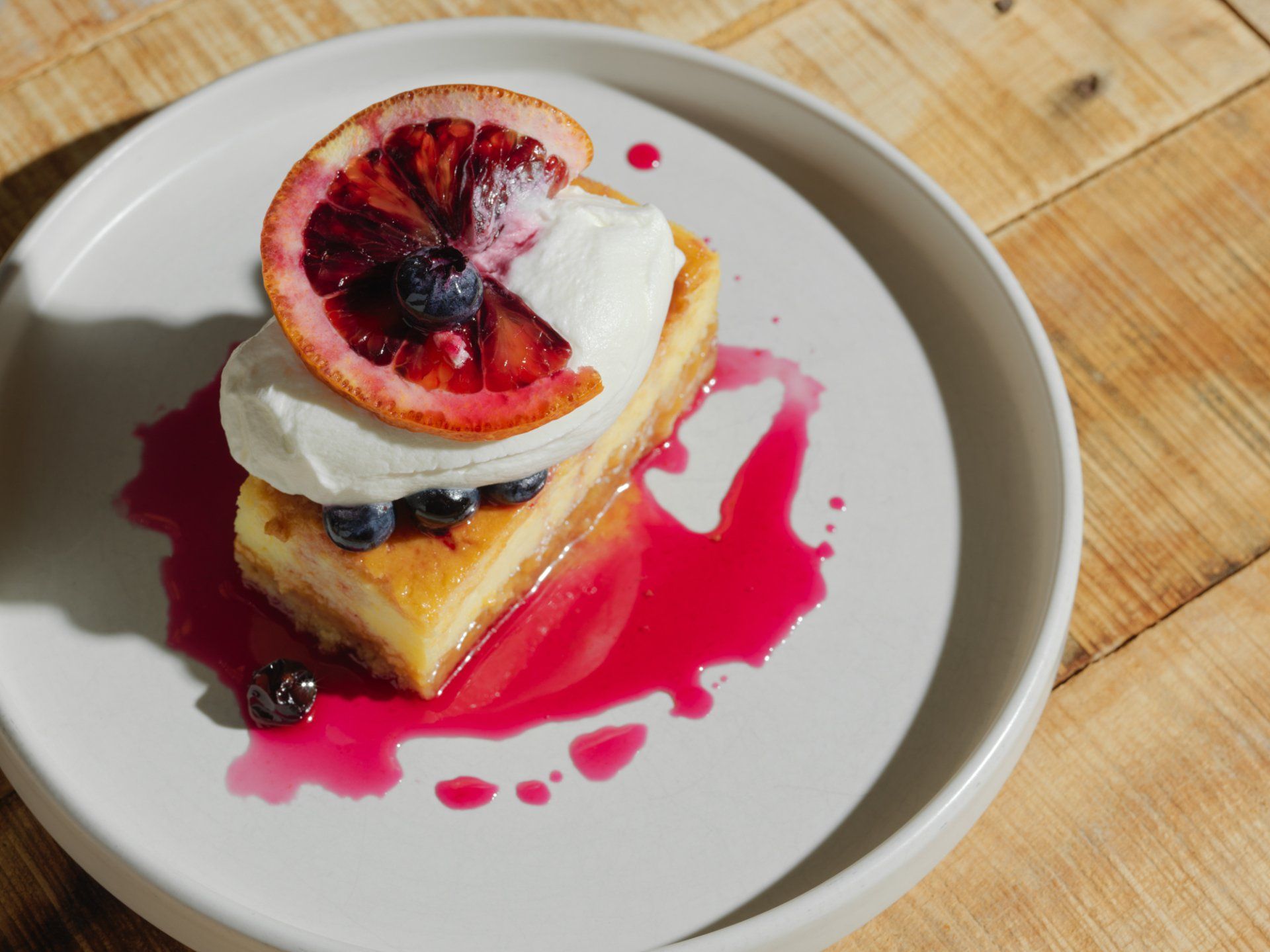 Slice of cake topped with blood orange on a white plate, drizzled with bright pink sauce