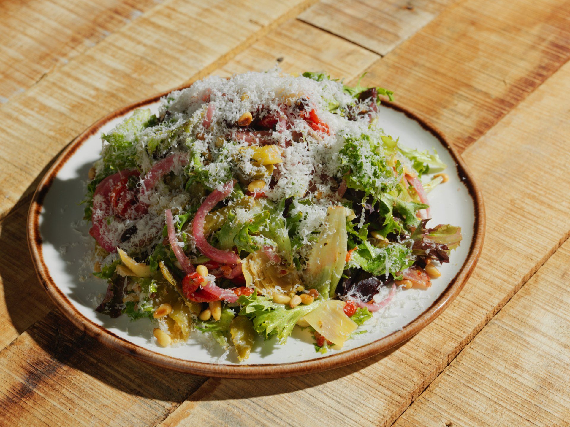 Colorful chopped salad with grated cheese on a white plate on a wooden table