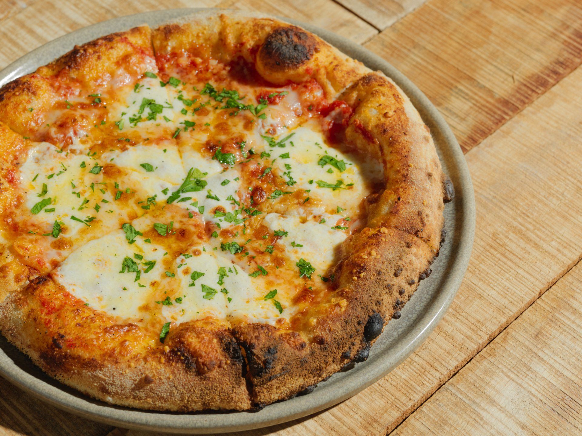 Cheese pizza on a metal tray, topped with herbs, sitting on a wooden table
