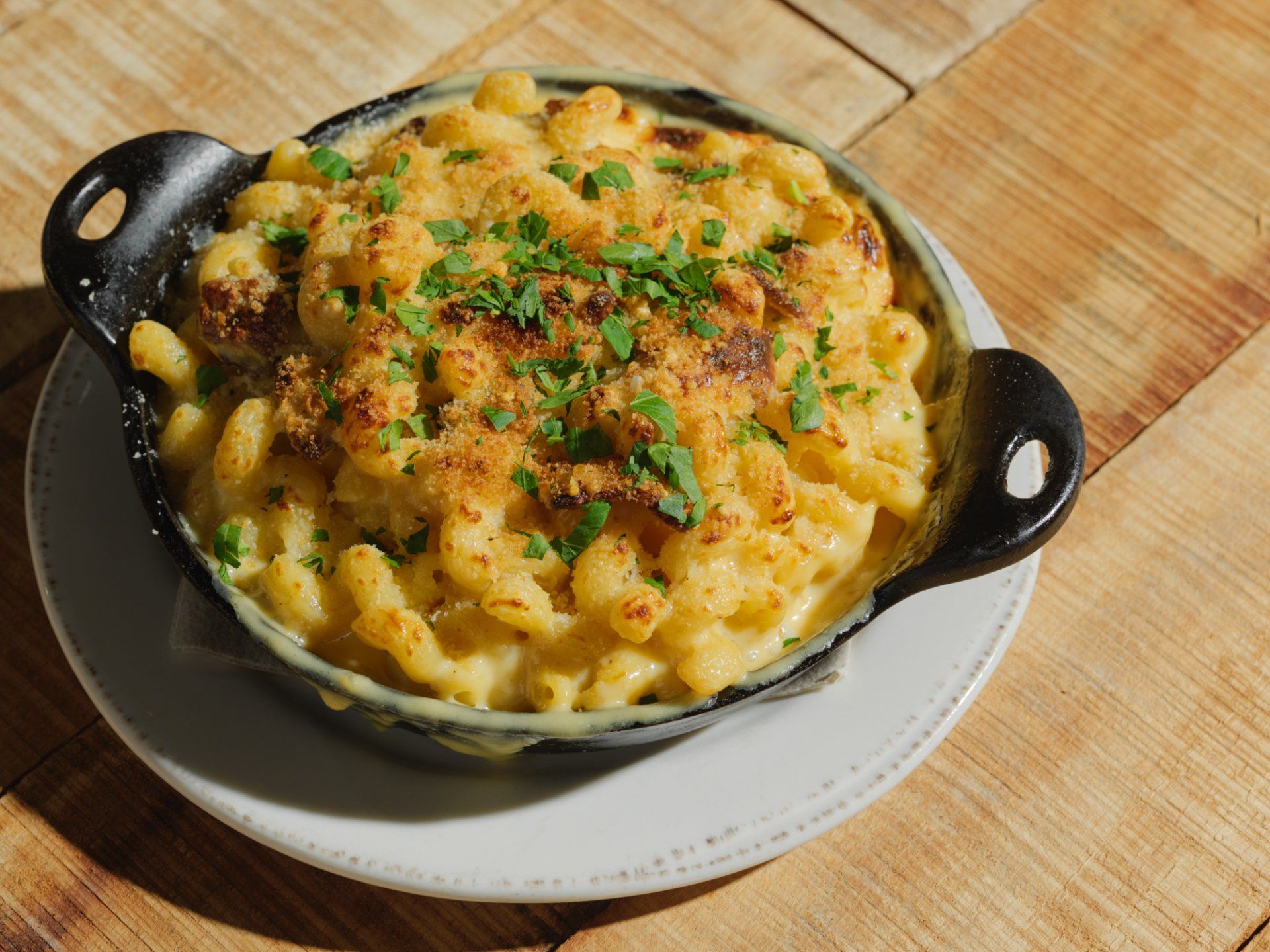 Baked macaroni and cheese in a black skillet, topped with herbs, on a white plate.
