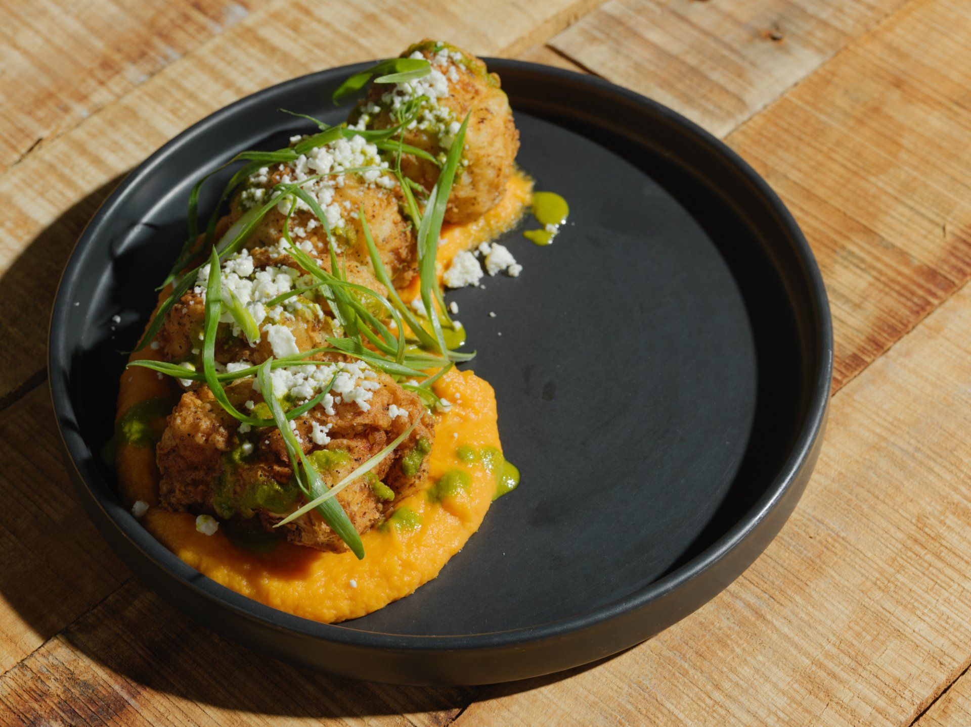Plated fried dish topped with herbs and crumbs, served on orange sauce on a black plate