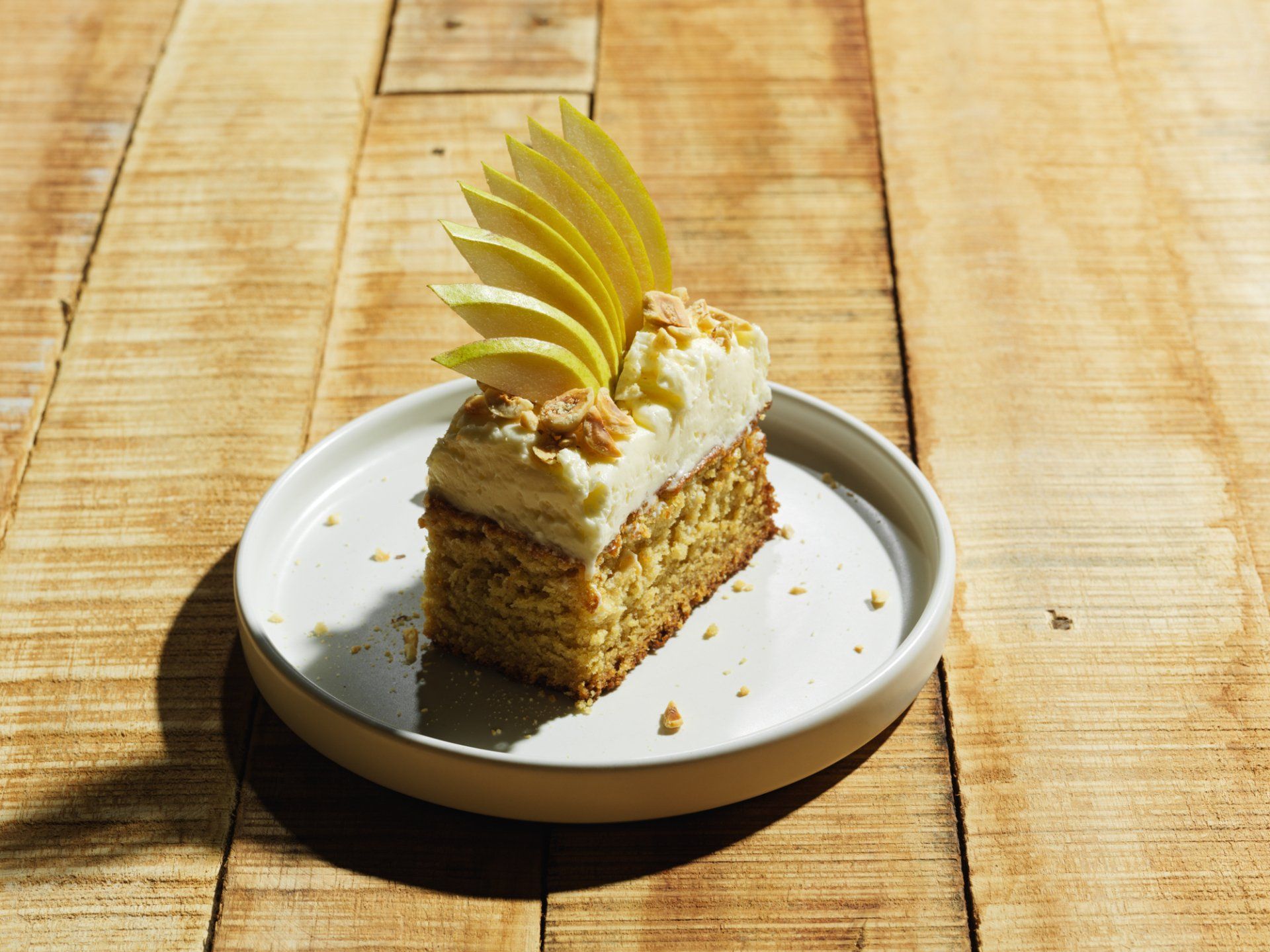 Slice of cake with white frosting and yellow garnish on a white plate on a wooden table.
