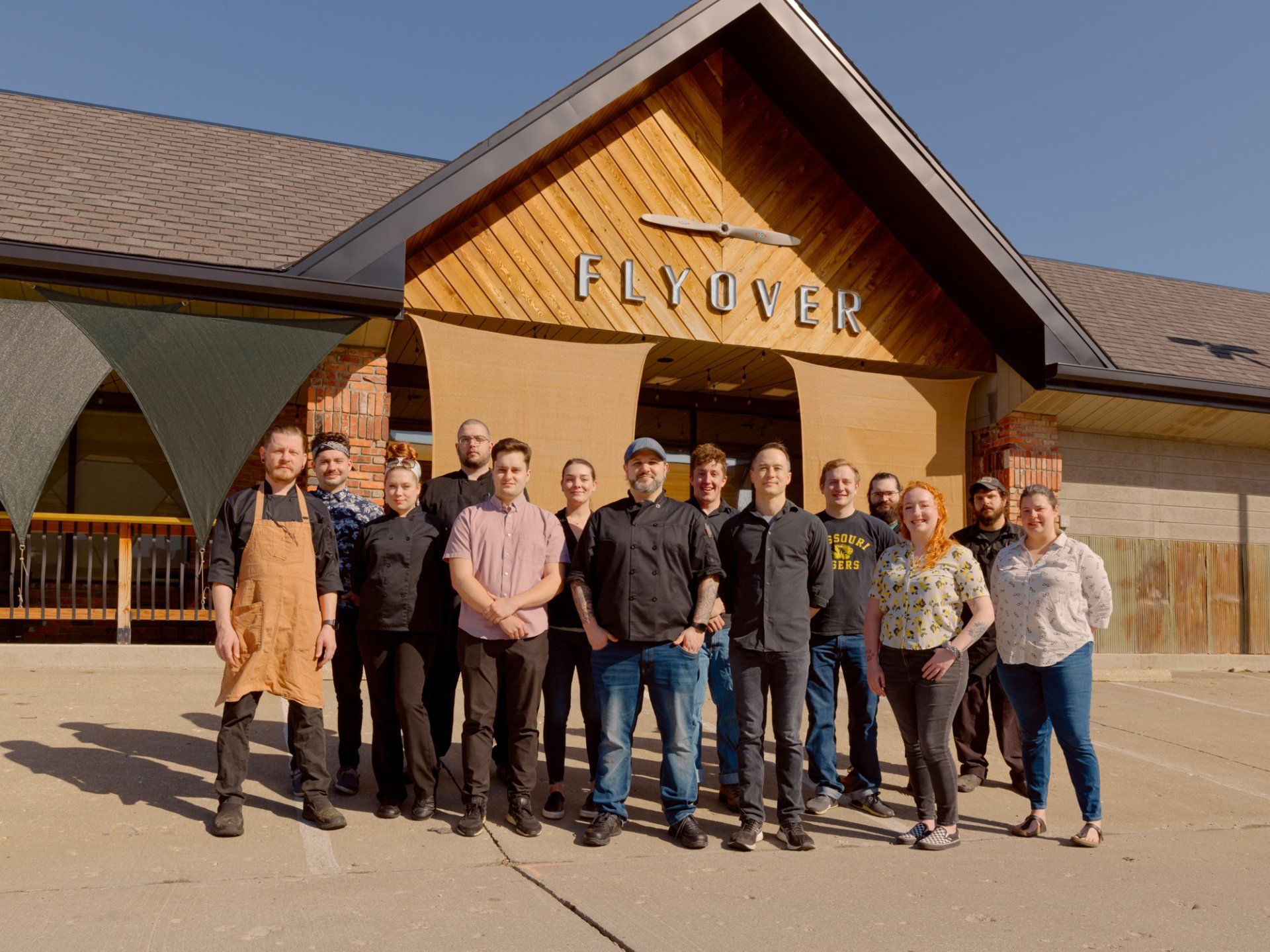 Group of people posing outside a wooden building with a “Fluver” sign under a clear sky