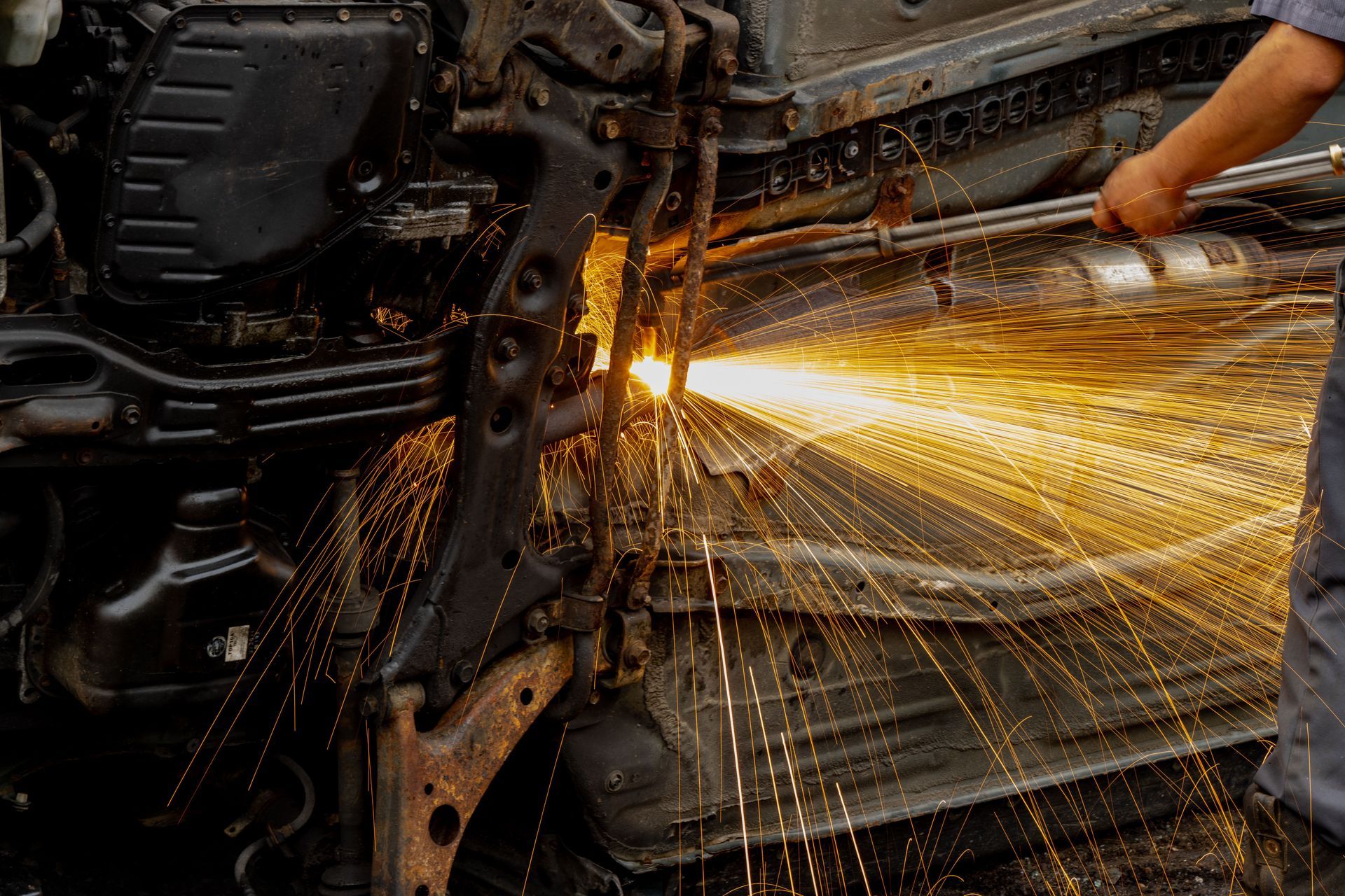 Worker using a grinder on a metal car frame, sending bright sparks across a workshop.