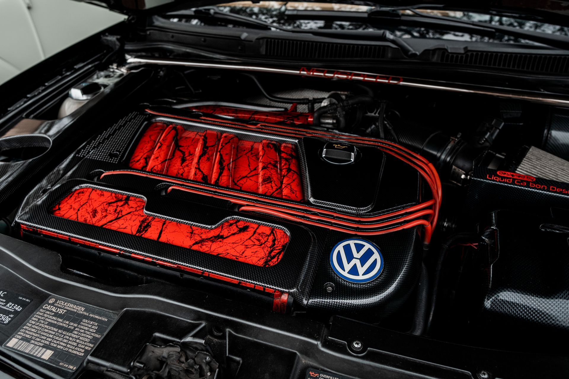 Volkswagen engine bay with a red-accented carbon-fiber engine cover and blue VW emblem