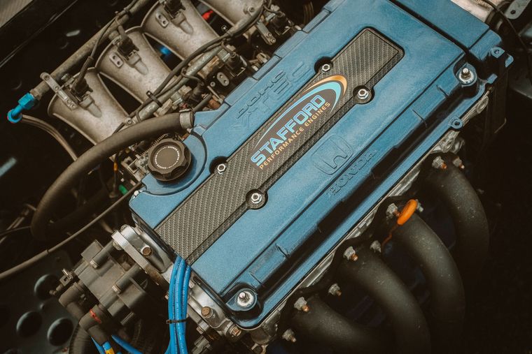 Close-up of a blue Honda engine with black intake manifold and metal components in a car bay