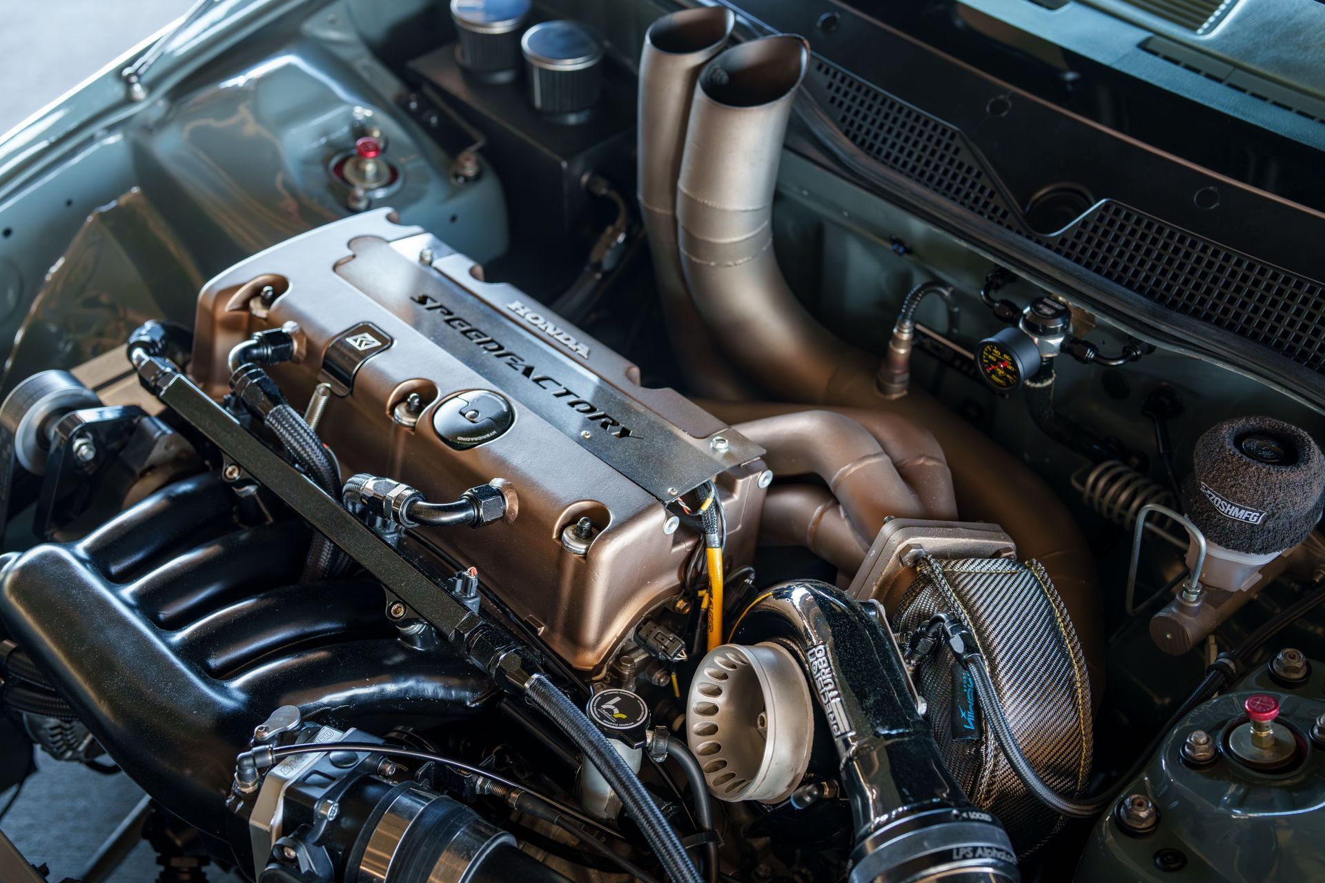 Modified car engine bay with exposed turbo piping, intake manifold, and belts, shown from above