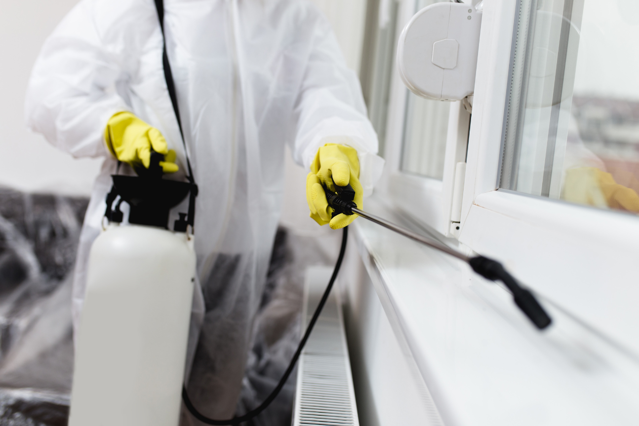 A man in a protective suit is spraying a window with a sprayer.