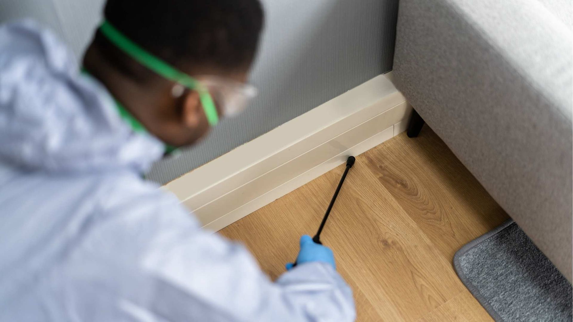 A man in a protective suit is spraying a wooden floor with a sprayer.